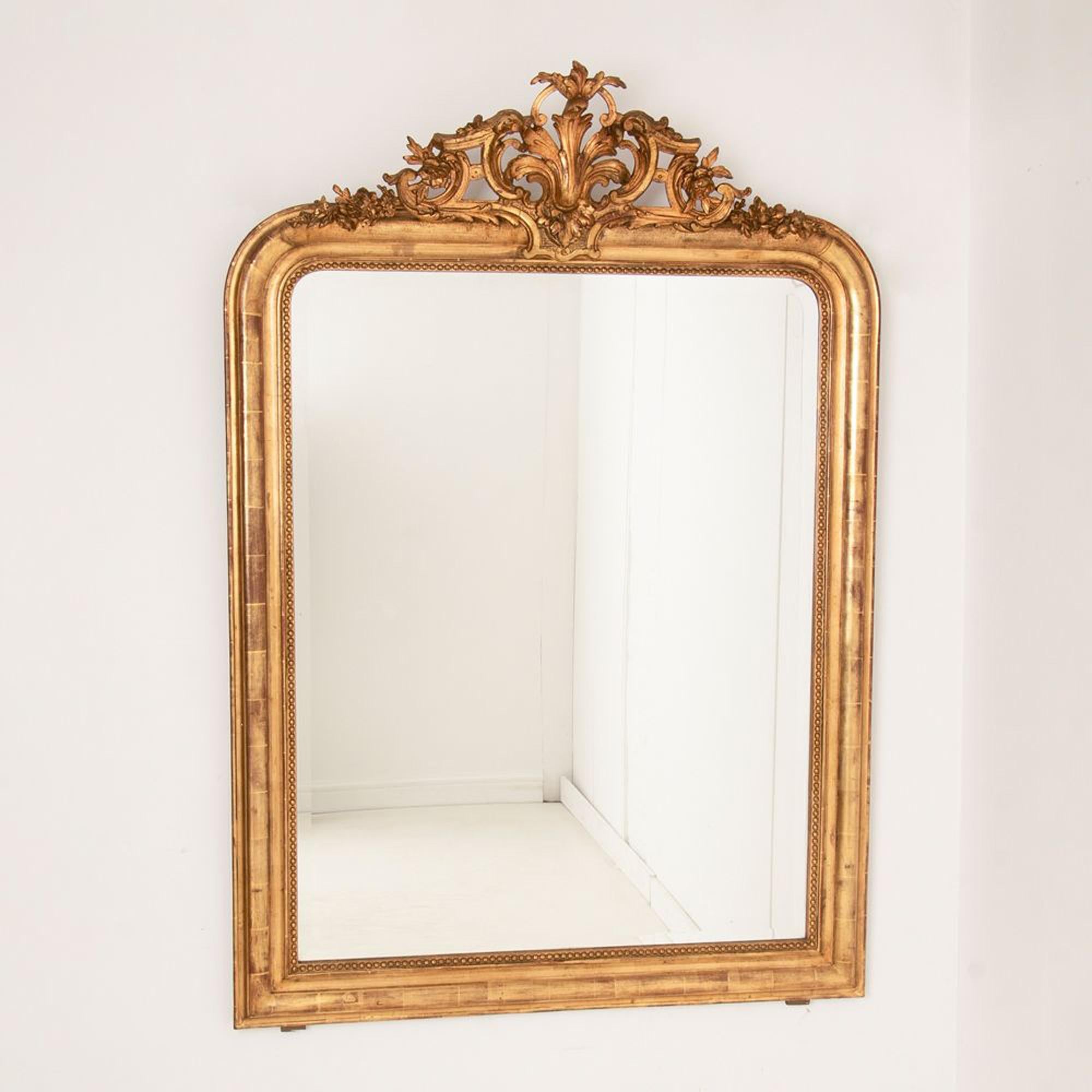 Large gilt on red overmantle crested Louis Philippe antique mirror. Finished in original two tone gilt worn through to red bole in places. Original bevelled glass. Original pine board back. Circa 1880.