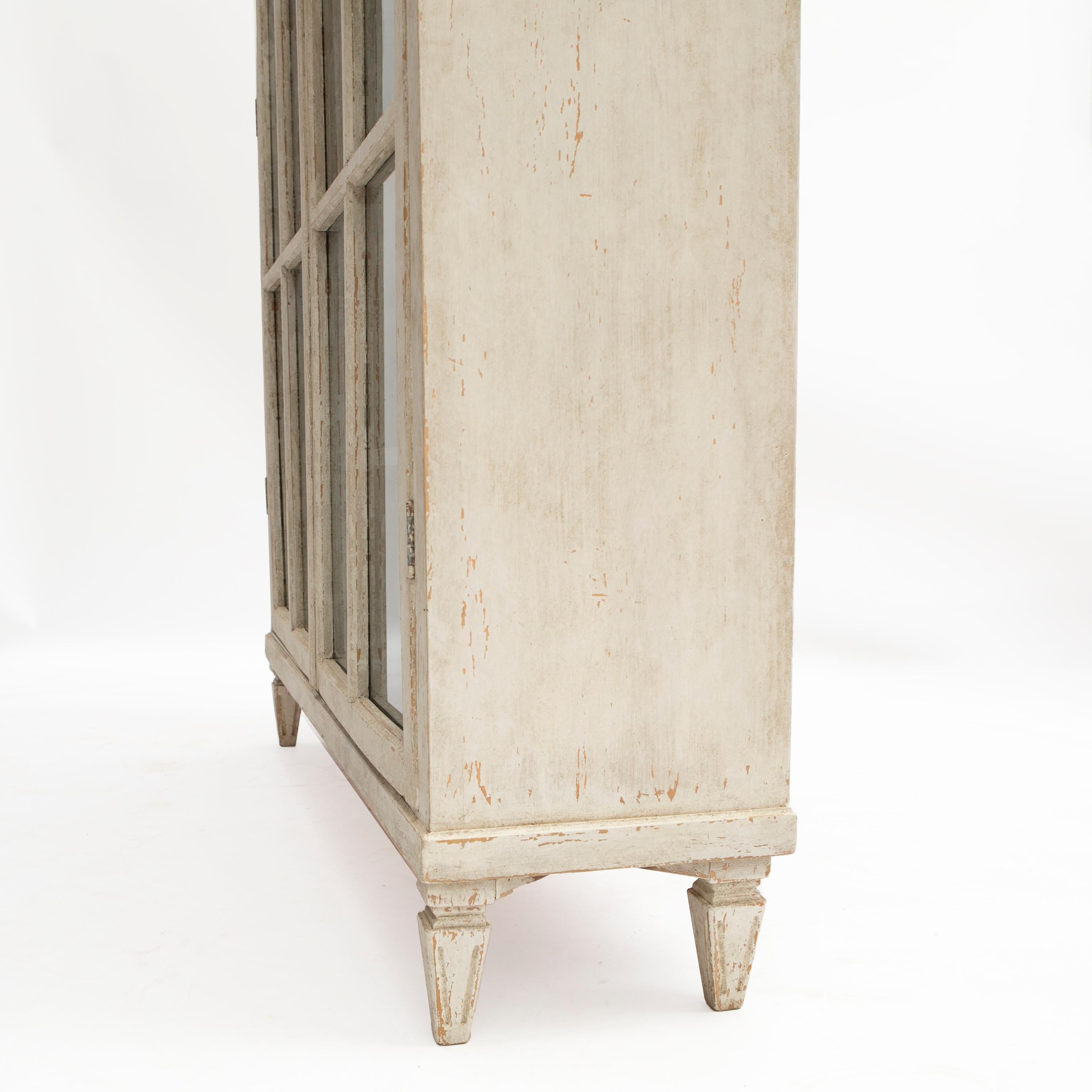 Elegant and large Swedish Gustavian style glazed vitrine or bookcase cabinet.

Professional painted finish in softly distressed Gustavian white, glass panel doors open to reveal a blue painted interior. Cornice featuring carved dentil and rhombuses