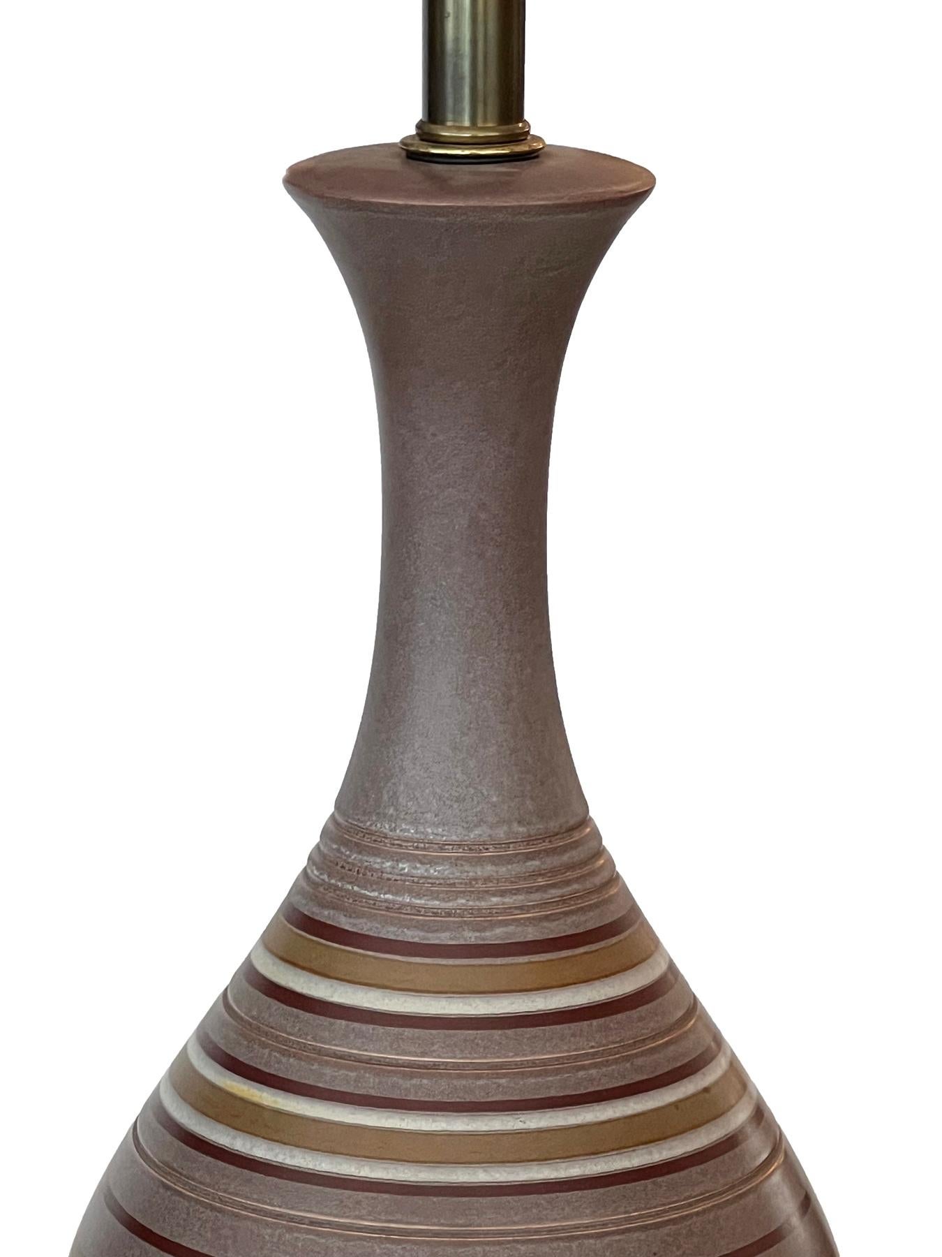chaque lampe de style saisissant présente un long col évasé au-dessus d'un corps ovoïde décoré de bandes périmétriques ivoire, brunes et ocre sur un fond tacheté de couleur ponce ; reposant sur des bases en noyer évasées avec des capuchons en laiton