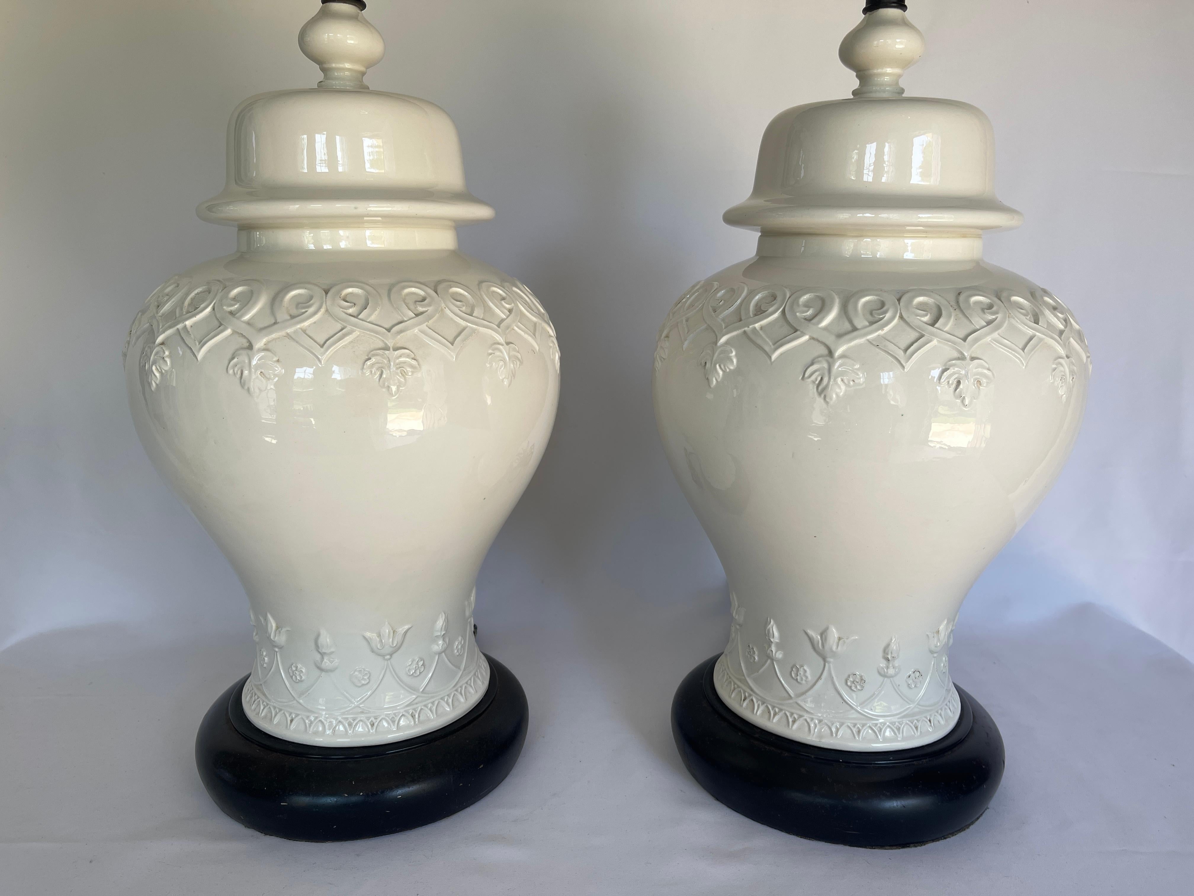 Large pair of Italian ceramic Blanc de Chine ginger jar lamps with white on white relief design all around. Black circular bases, have some finish loss.
Original solid brass acorn finials included.
Chinoiserie lamp body measures 19