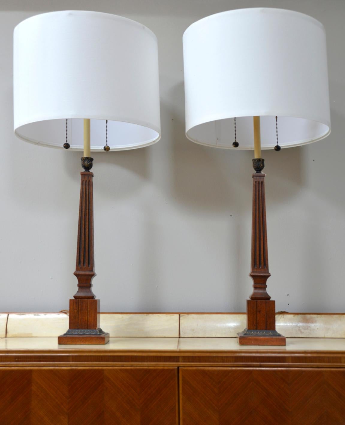 Ein sehr elegantes Paar korinthischer Säulenlampen im Empire-Stil auf einem quadratischen, abgestuften Sockel. Das schwarze Kapitell ist mit Blättern verziert und hat cremefarbene Metallfassungen für die Glühbirnen, an denen Messingkugelketten