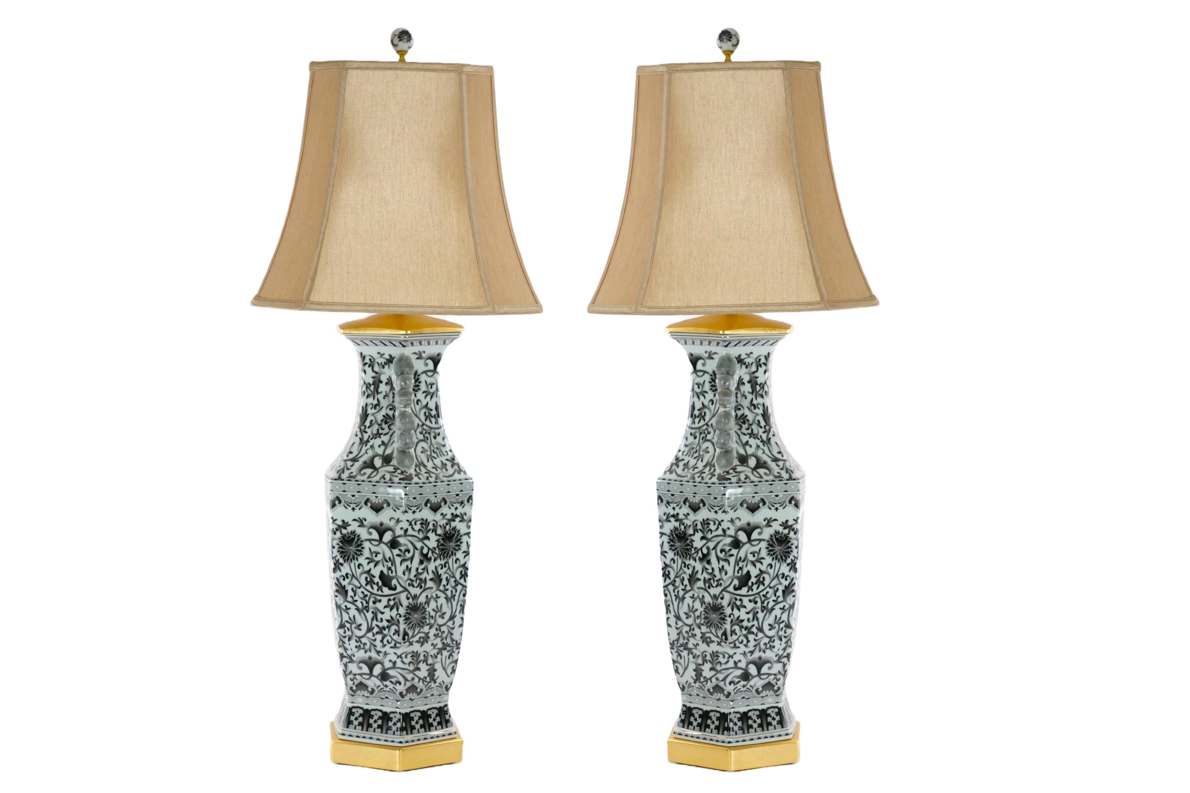 Beautifully hand painted and decorated large glazed tapestry porcelain pair table lamps. Each lamp features an hand decorated and painted black tapestry with white background design, with two side handles in a geometric shape form resting on a gilt