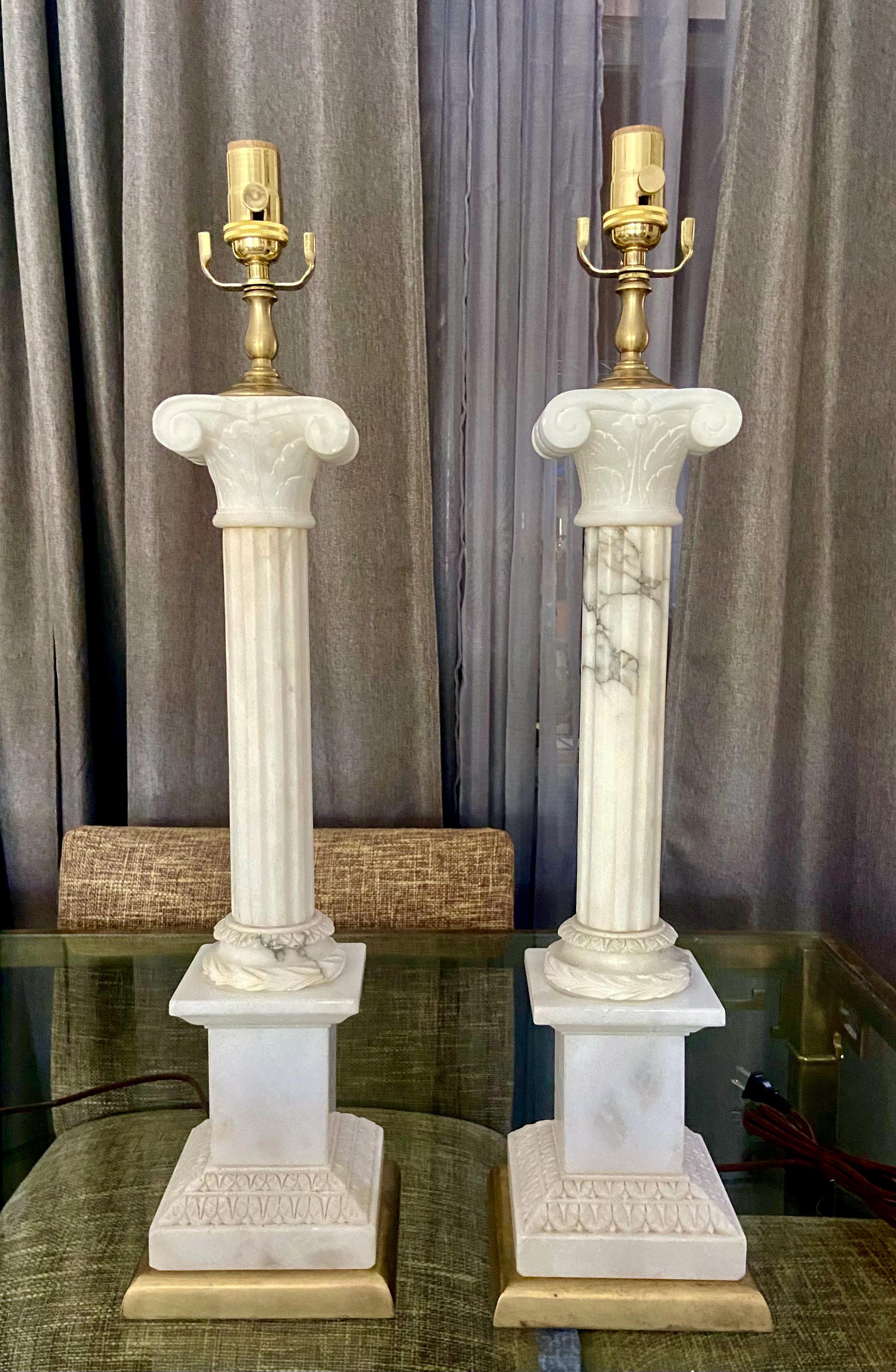 Pair of large scale finely crafted hand carved neoclassical style column form alabaster lamps on brass bases. Expertly crafted with intricate carving throughout. Newly wired with new brass 3 way sockets and rayon cords. Shades are not