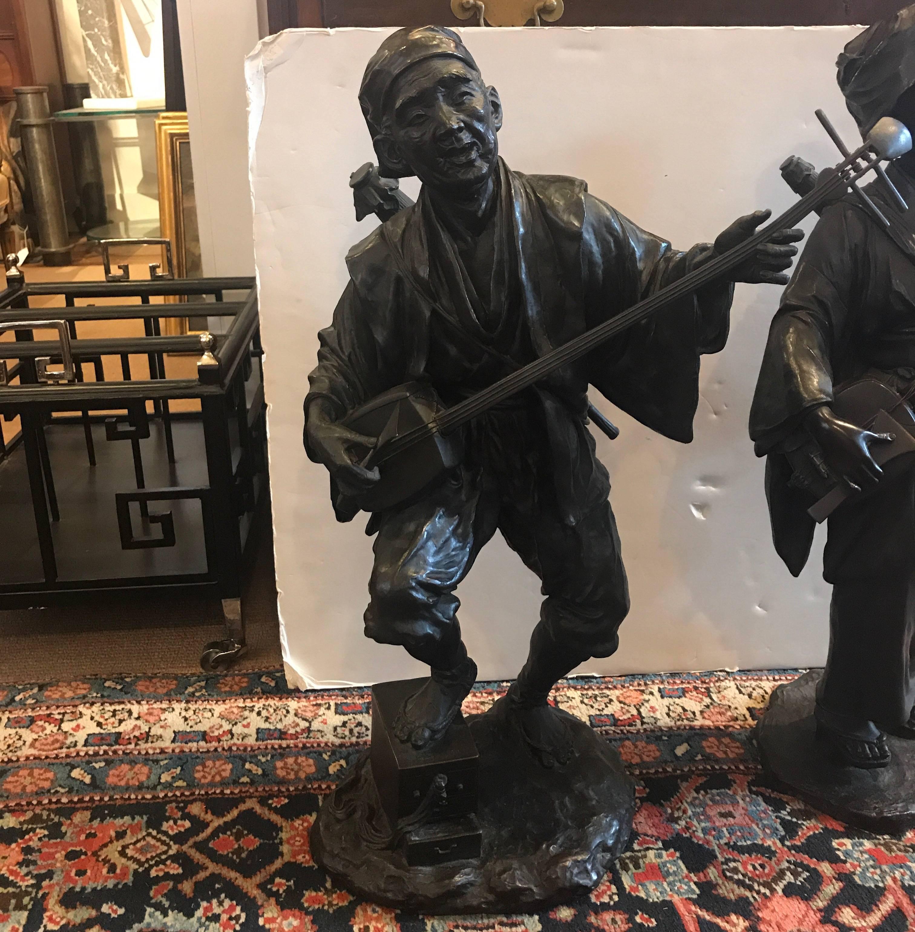A pair of male and female Japanese Meiji period figures of musicians playing a shamisen with finely detailed castings. Each one with a Japanese signature on the base and having their original patination.