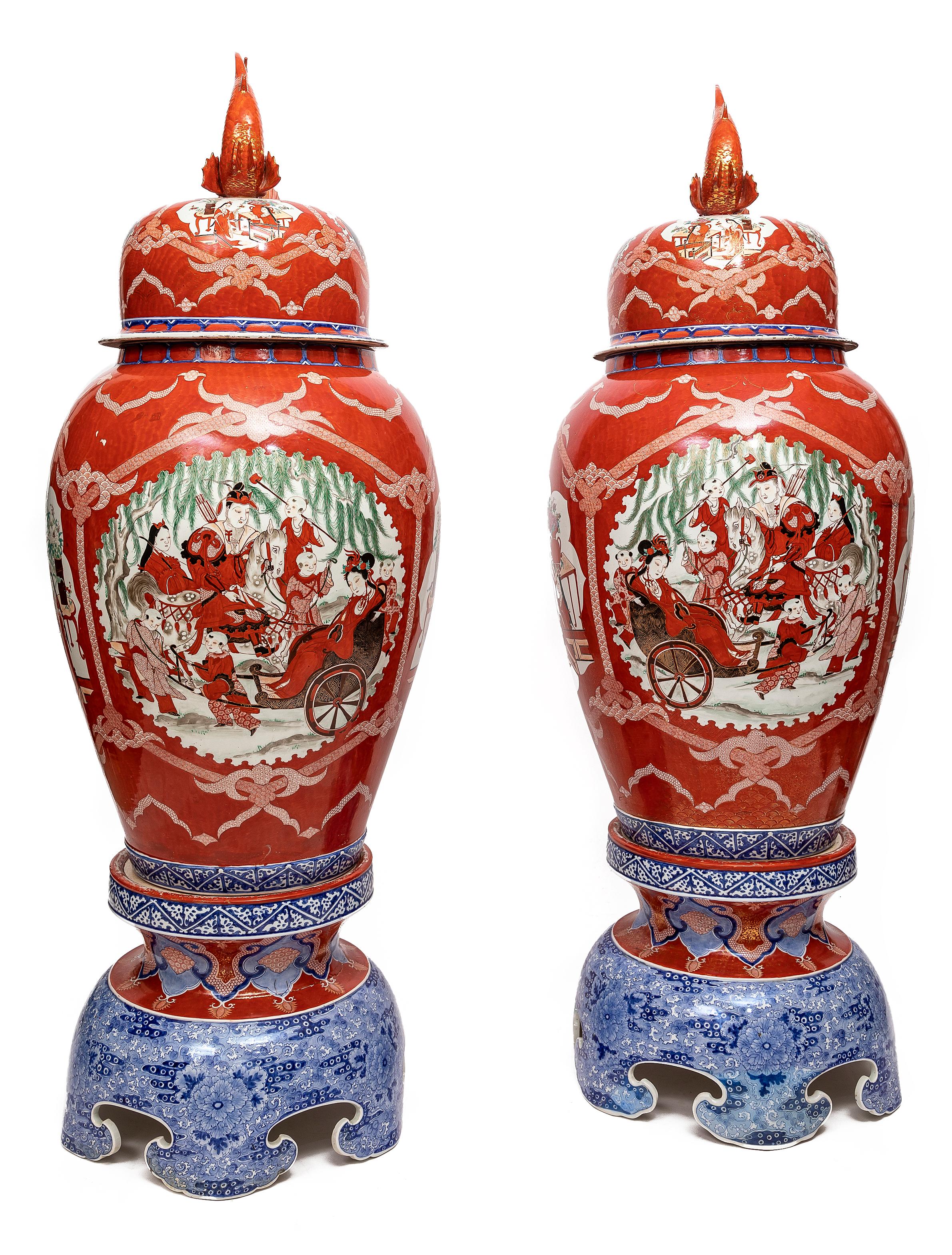 A Monumental and Very Rare Pair of Japanese Coral Ground Imari Covered Vases on Stands, from the Getty Collection.  Each painted to the front and back with a gentleman on horseback, a lady in a rickshaw and numerous children and attendants, the