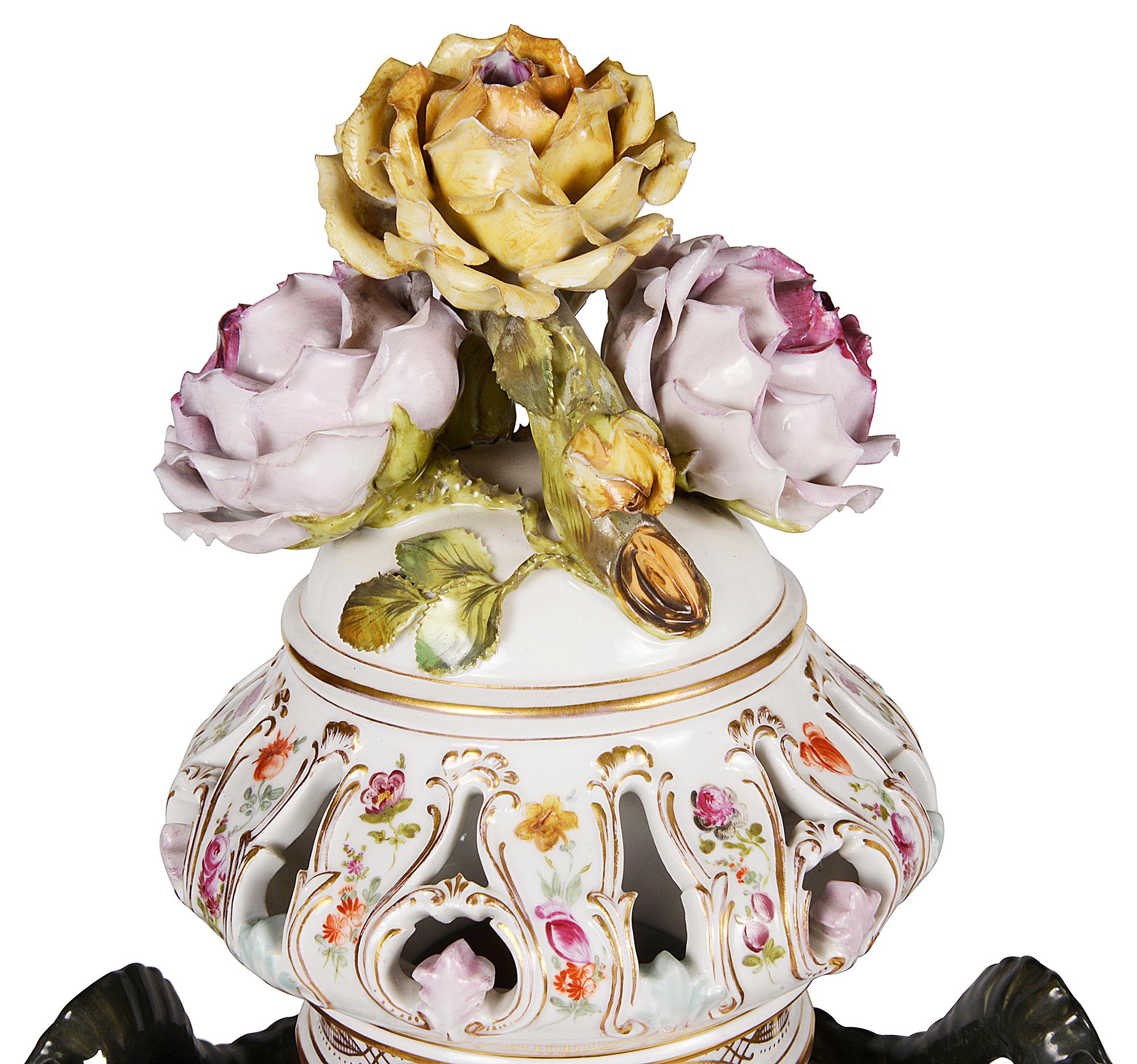 A very impressive and decorative pair of Meissen style lidded porcelain vases. Each with floral encrusted decoration to the pierced lids, Rams head handles to either side, classical romantic hand painted scenes and raised on pedestal bases.