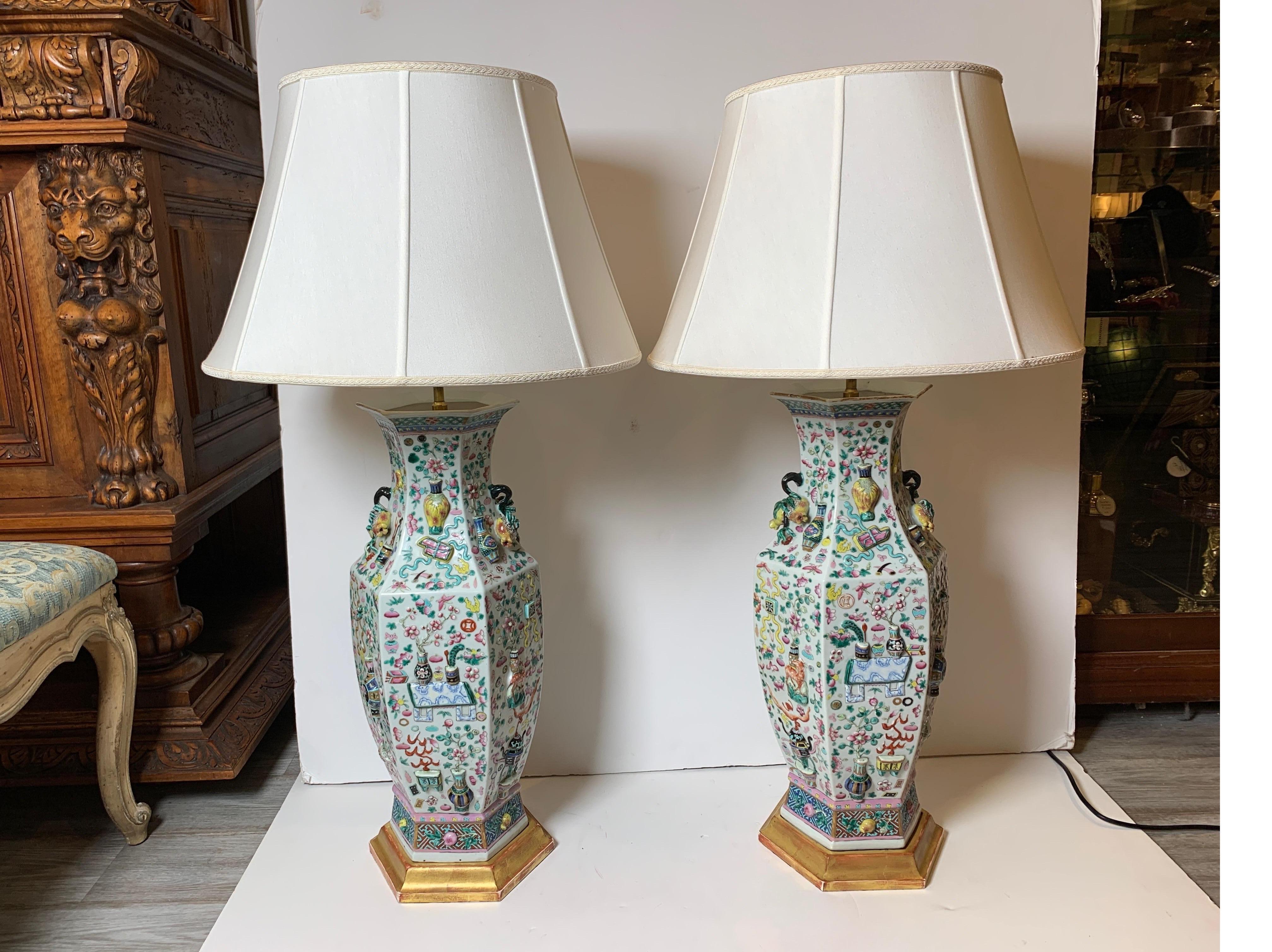 Best quality high relief hand painted Chinese export porcelain lamps. The vases from the early 19th century, now as lamps with giltwood bases. The center pole is adjustable to accommodate different size shades, with two electric sockets. The shades