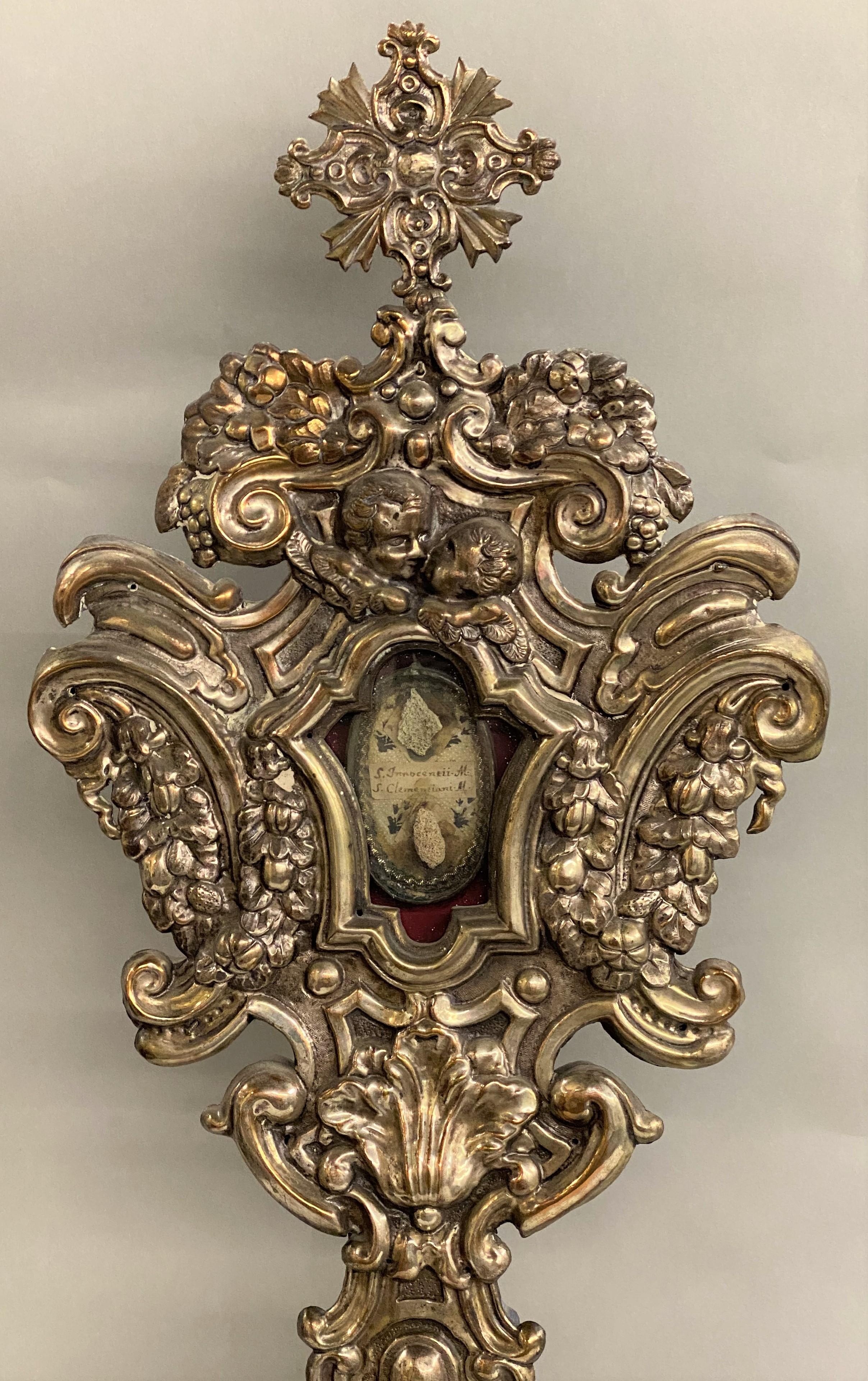 A fine large pair of Italian silvered metal over wood reliquaries with putti, grape, shell, and scrollwork design. Each have memorial pendant displays with names (The left reads S. Innocentii M & S Clementiani M,” while the other is illegible. The
