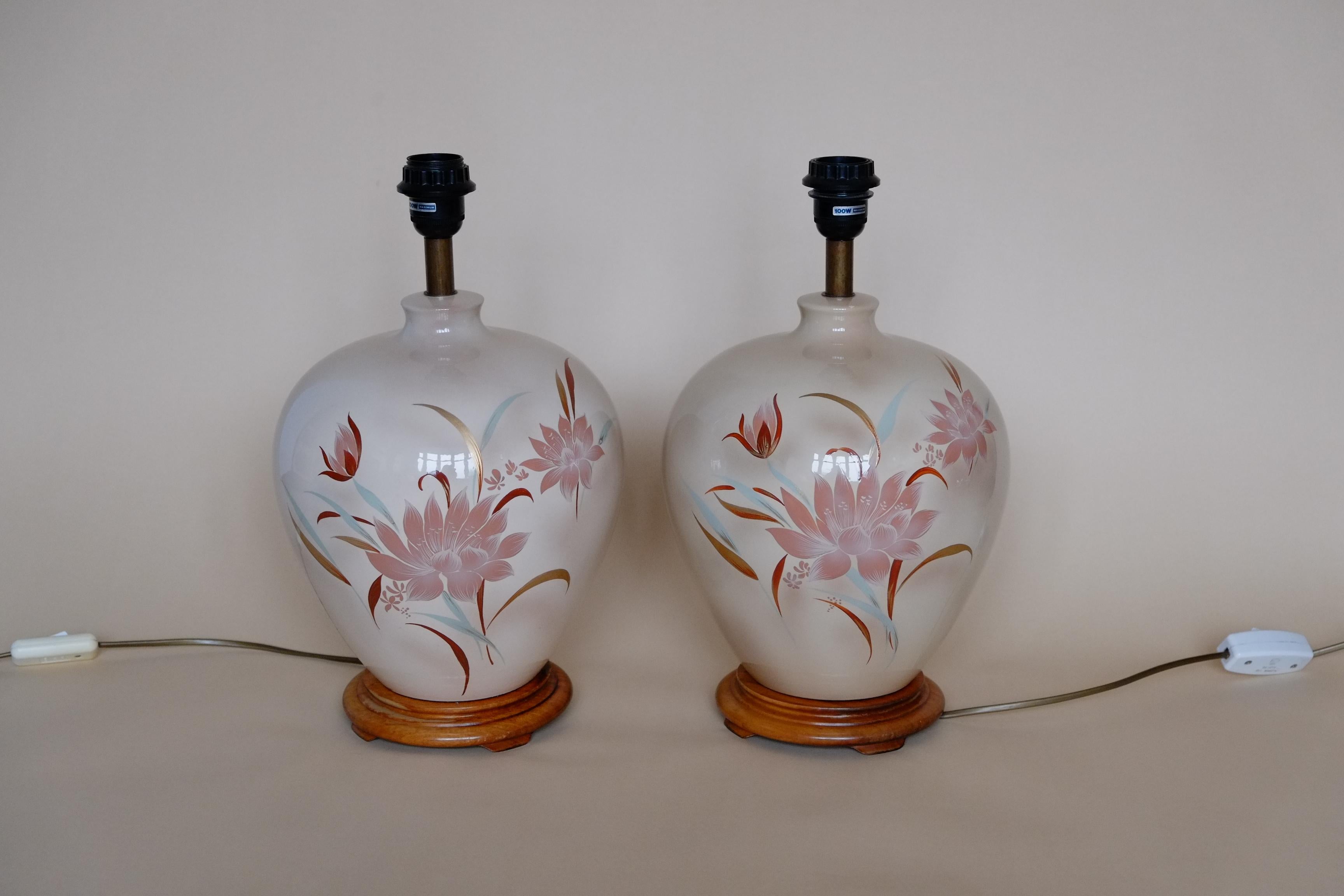 A beautiful pair of large ceramic lamps with a floral motif. The lamps have a wonderful bulbous ginger jar shape on a wood base. Finished in a glossy peachy plaster tone with muted pinks, mint green and pale gold floral decoration. The floral