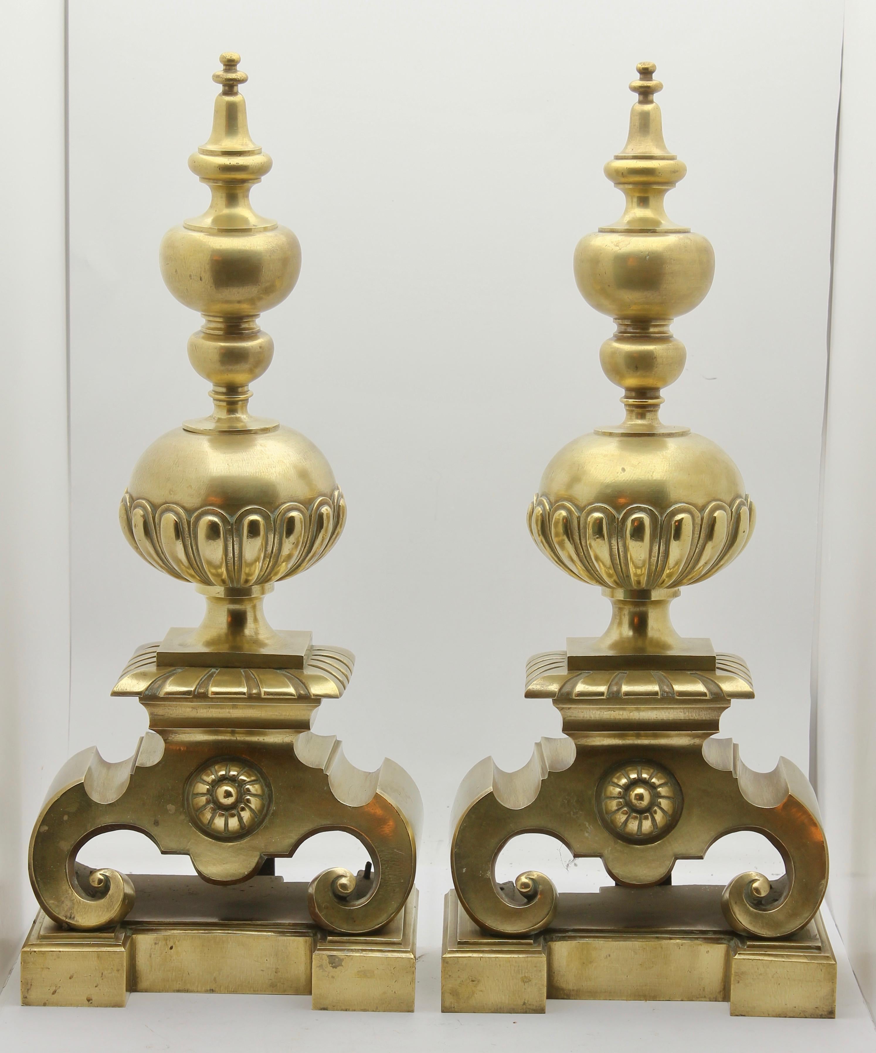 Sometimes referred to as 'fire dogs', these heavy brass andirons can be simply attached to a fire basket of hearth furniture, giving that classical country-home look.
The scrolled foot on the base supports a half-gadrooned ball and finial. The back