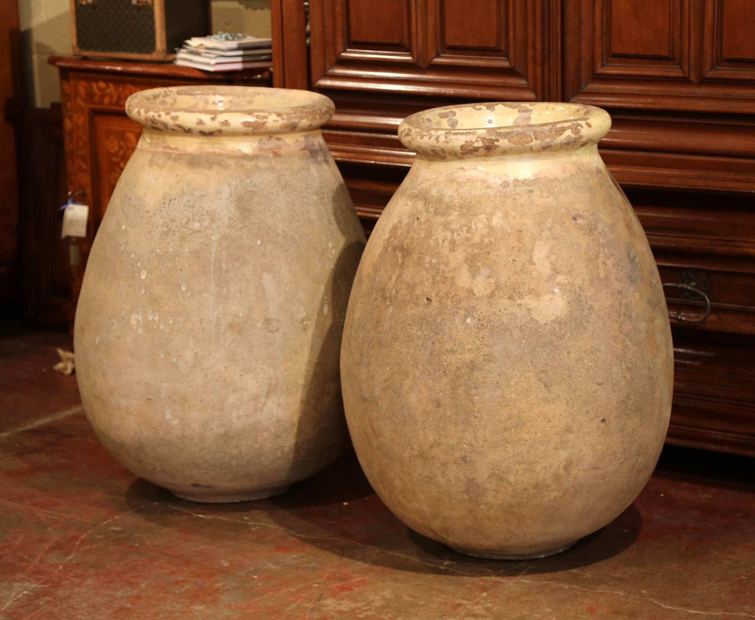 This large pair of earthenware olive jar was created in Southern France, circa 1870. Round in shape, both antique vases have a neutral beige color finish embellished by a yellow glaze around the neck and trim. Overall, these traditional jars are in