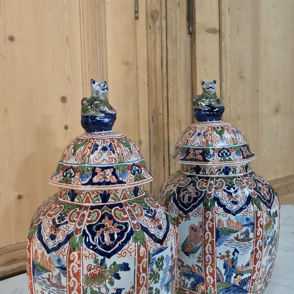 Pair of 19th century large delft vases feature vivid coloration underglaze cobalt blue and manganese red with chinoiserie scenes painted in panels and preserved by the proprietary glaze developed in the region hundreds of years ago. Completely