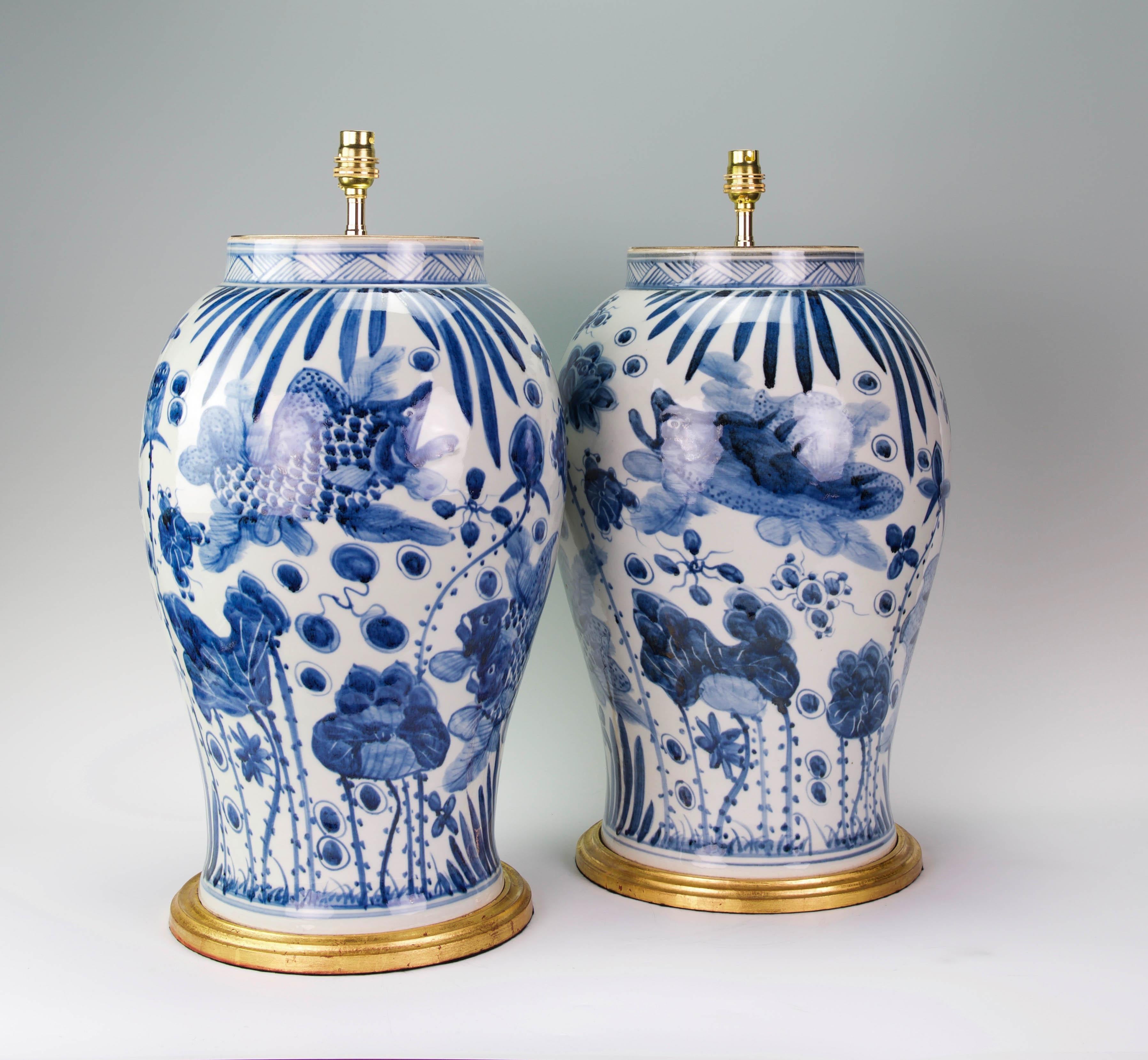 A fine pair of large Chinese blue and white vases decorated throughout in the Kangxi style, with superb fish and aquatic plants in tones of blues on a white ground, now mounted as lamps with hand gilded turned bases.

Height of vases: 18 1/2 in
