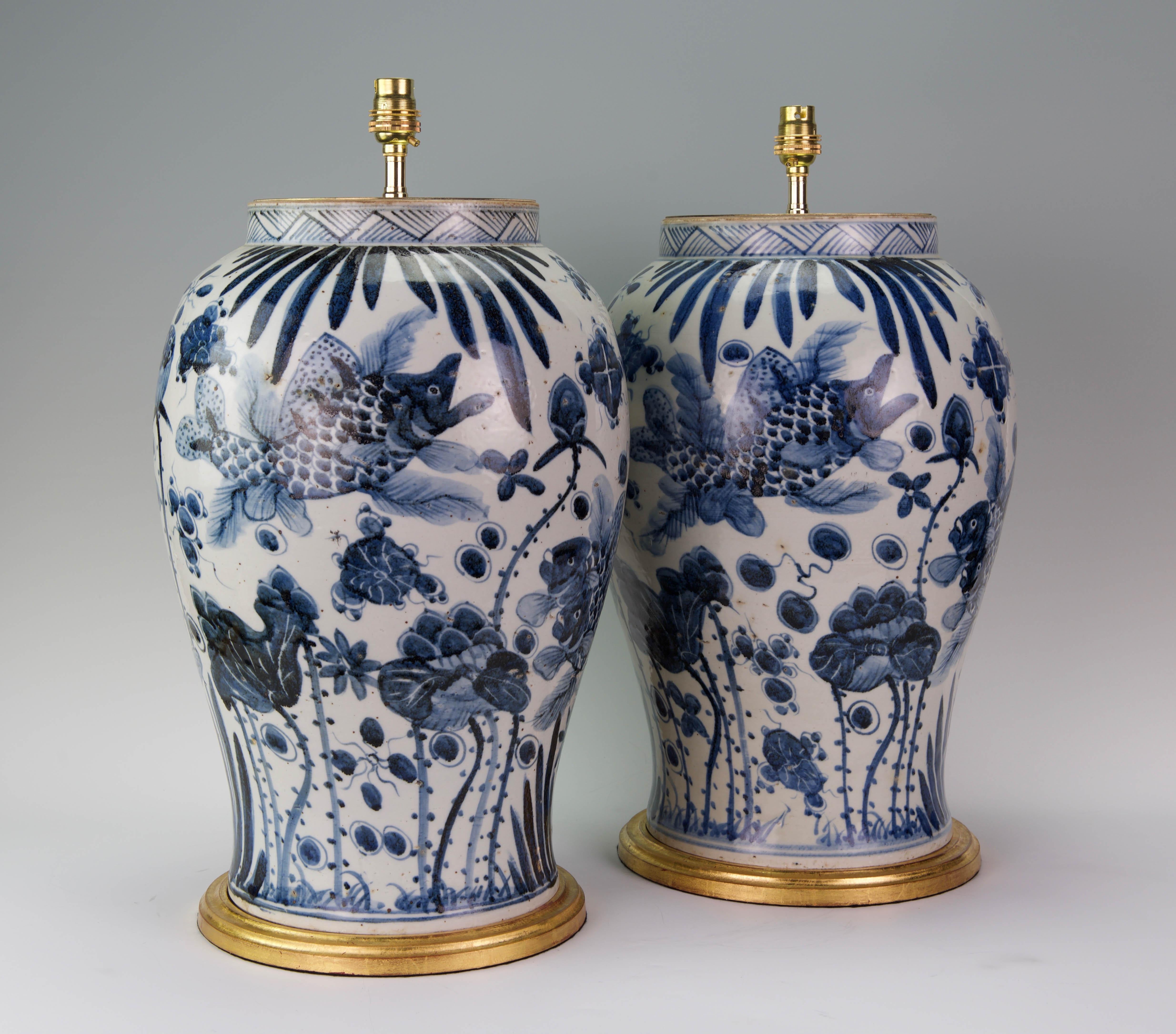A fine pair of large Chinese blue and white vases decorated throughout in the Kangxi style, with superb fish and aquatic plants in tones of blues on a white ground, now mounted as lamps with hand gilded turned bases.

Height of vases: 18 in (46
