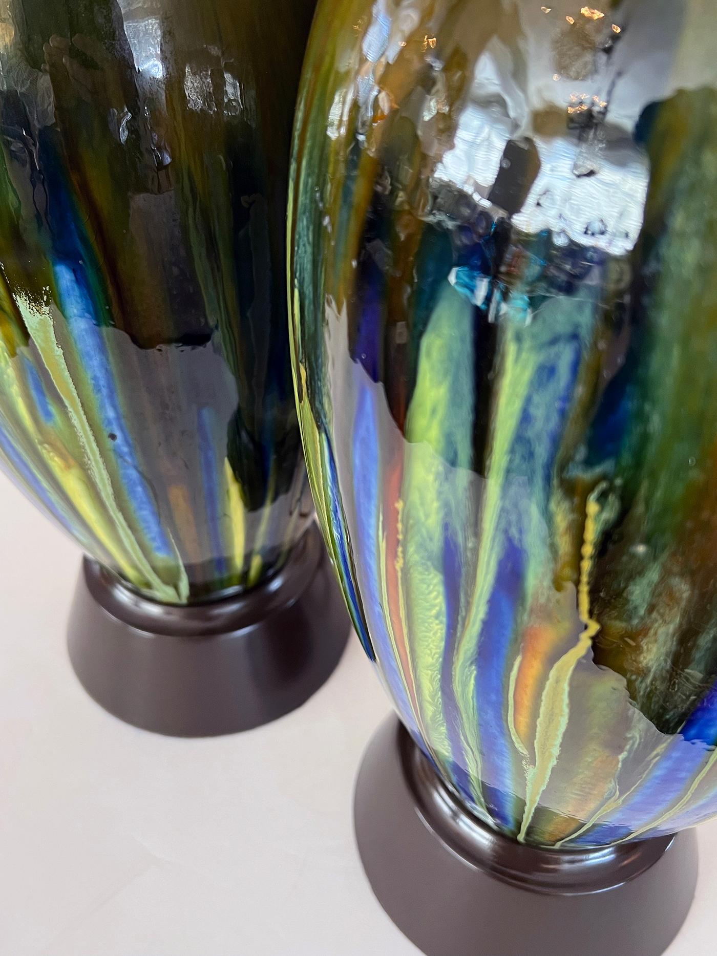 Each tall lamp of ovoid form with rich drip-glaze surface in colors of blue, green, yellow, sienna and brown; each resting on brown painted metal bases.