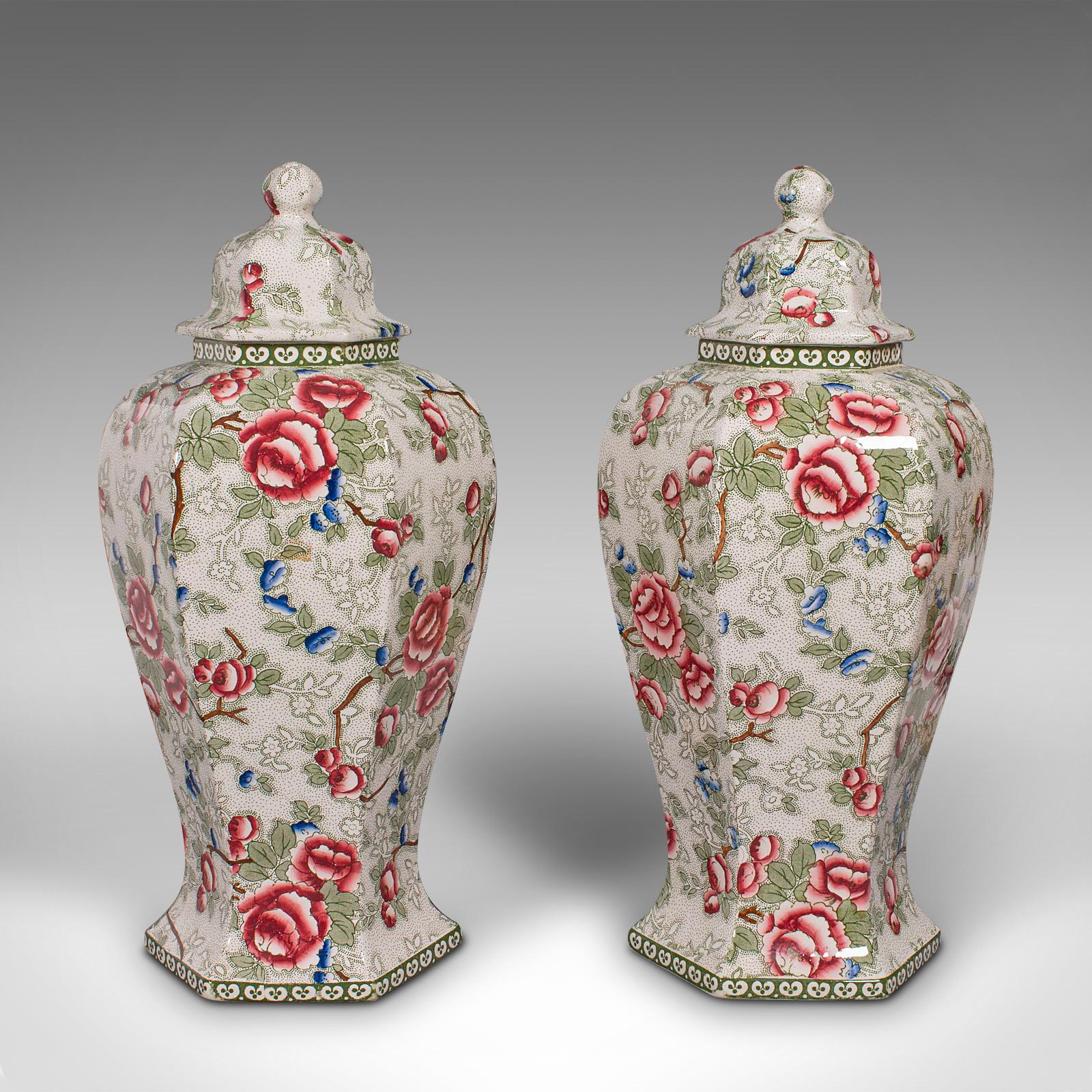 This is a large pair of antique baluster urns. An English, ceramic decorative lidded jar or vase, dating to the early 20th century, circa 1920.

Striking hexagonal forms and profusely detailed in Chinese Rose taste
Displaying a desirable aged