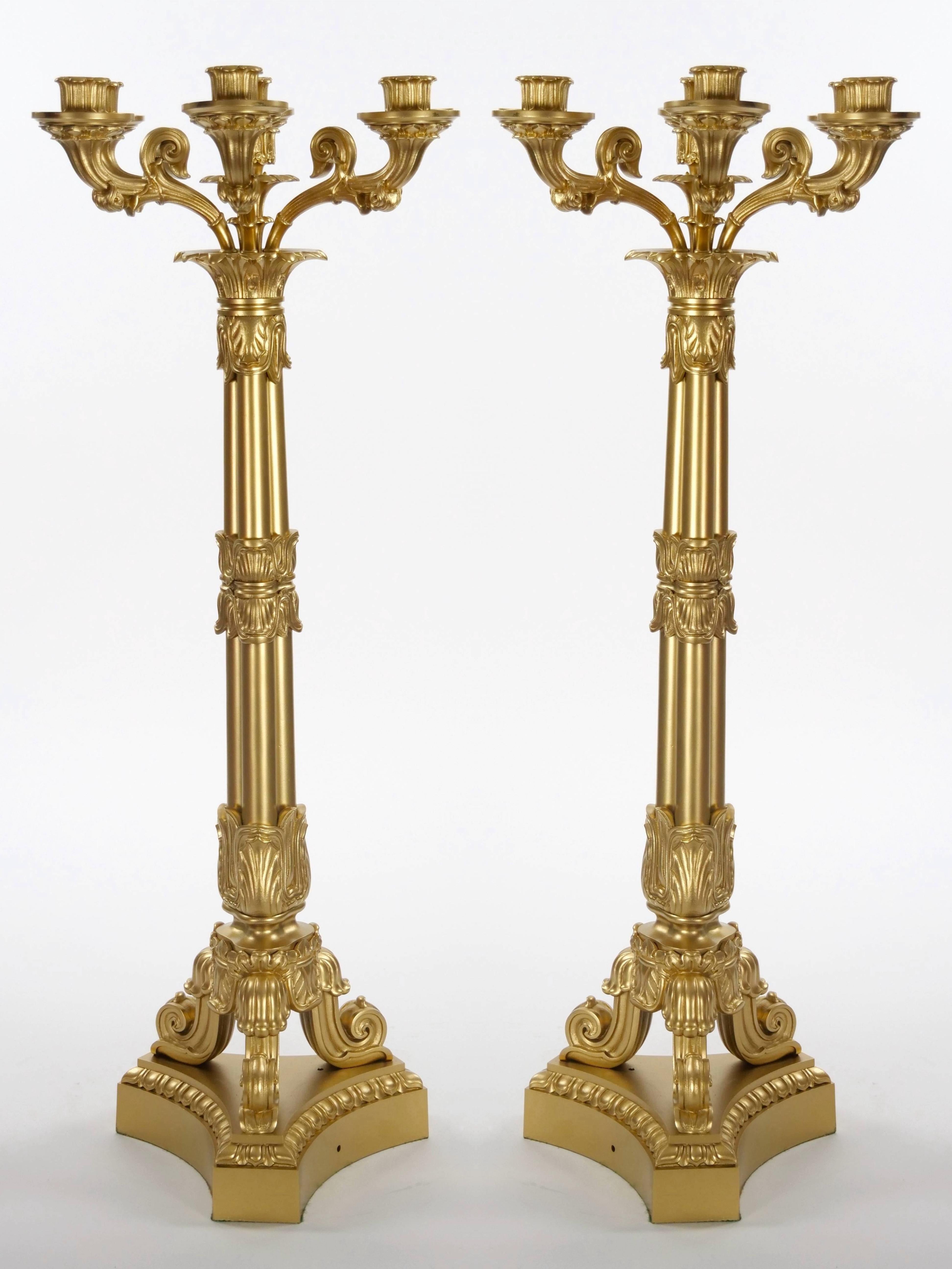 This noble pair of antique Charles X style French bronze candelabra are a stunning representation of refined craftsmanship and elegance. Each candelabrum is raised on trefoil bases, supported by three intricately decorated stylized feet. The
