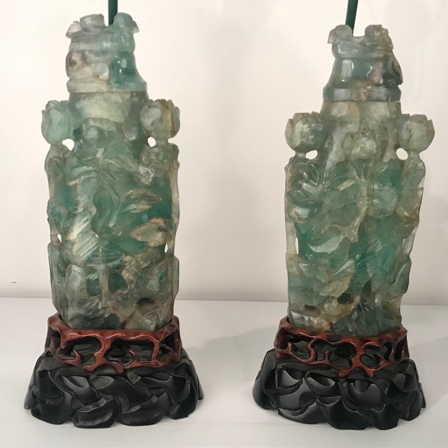 This pair are carved in relief with birds, leaves and flowers, raised on wooden pierced and simulated rocky bases They are mounted as lamps. The shades are reminiscent of oriental pavilions and the antique jade finials are in pierced