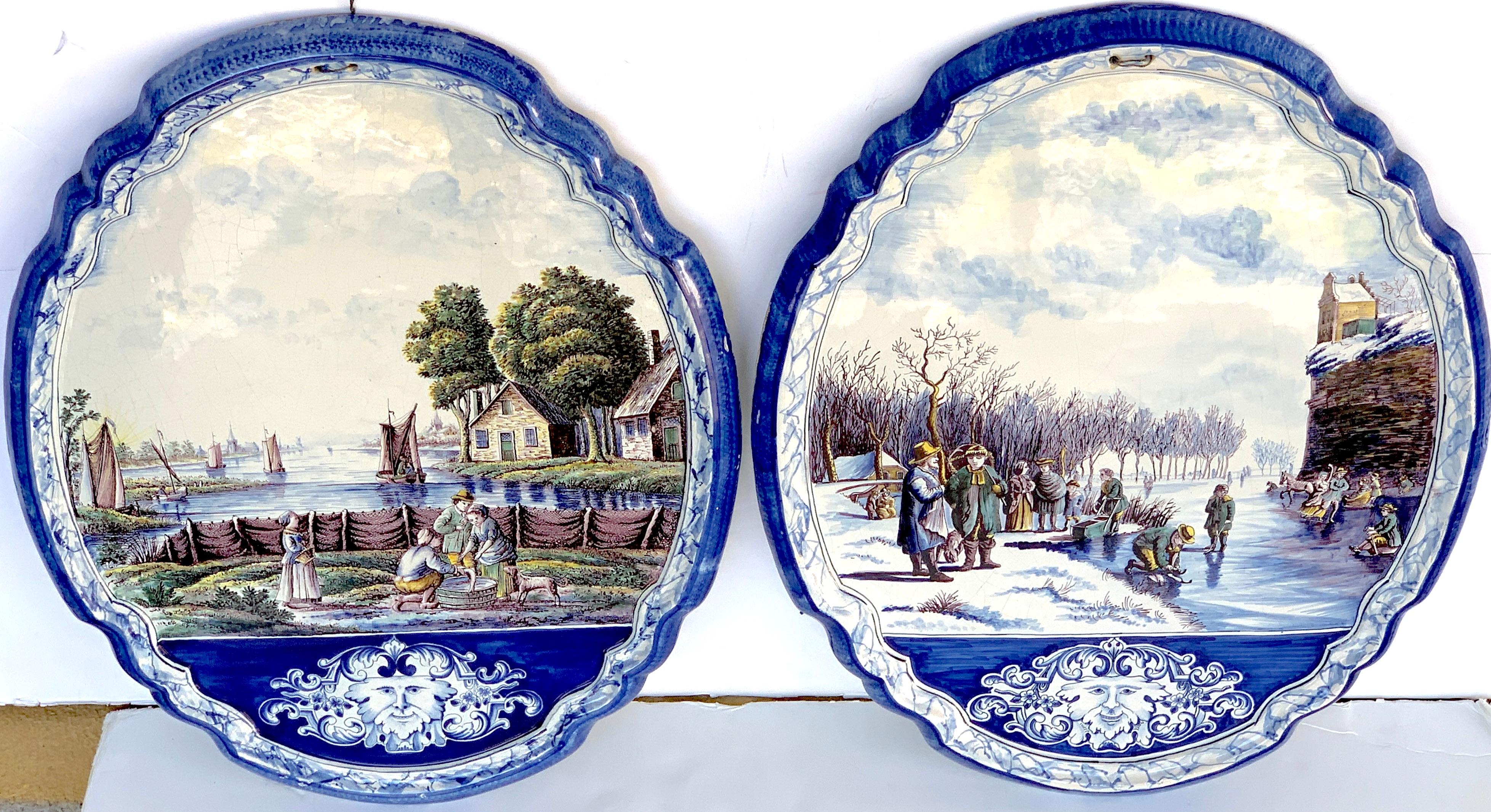 Large pair of antique delft topographical wall plaques, each one decorated in blue and white with landscapes, one a winter lake scene, the other summer lake view, both with a medallion at the bottom of the plaque. Each one signed on back 