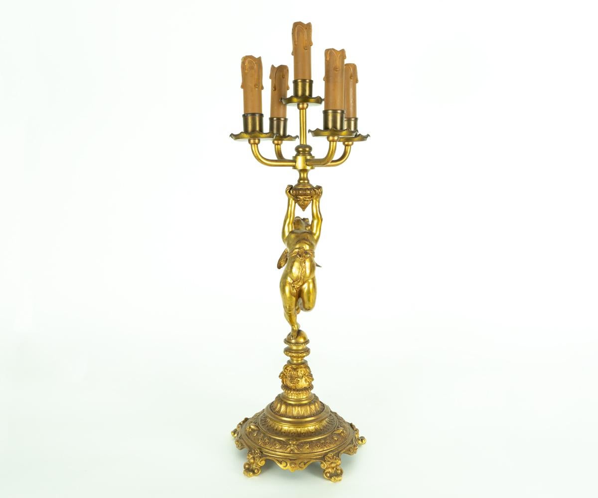 This pair of candlesticks are antique and gilt bronze. The angel, Cherub figure is the centerpiece of the stem which supports the five arms on each stick. They both rest upon an intricately cast base. These had at one time been wired for electric