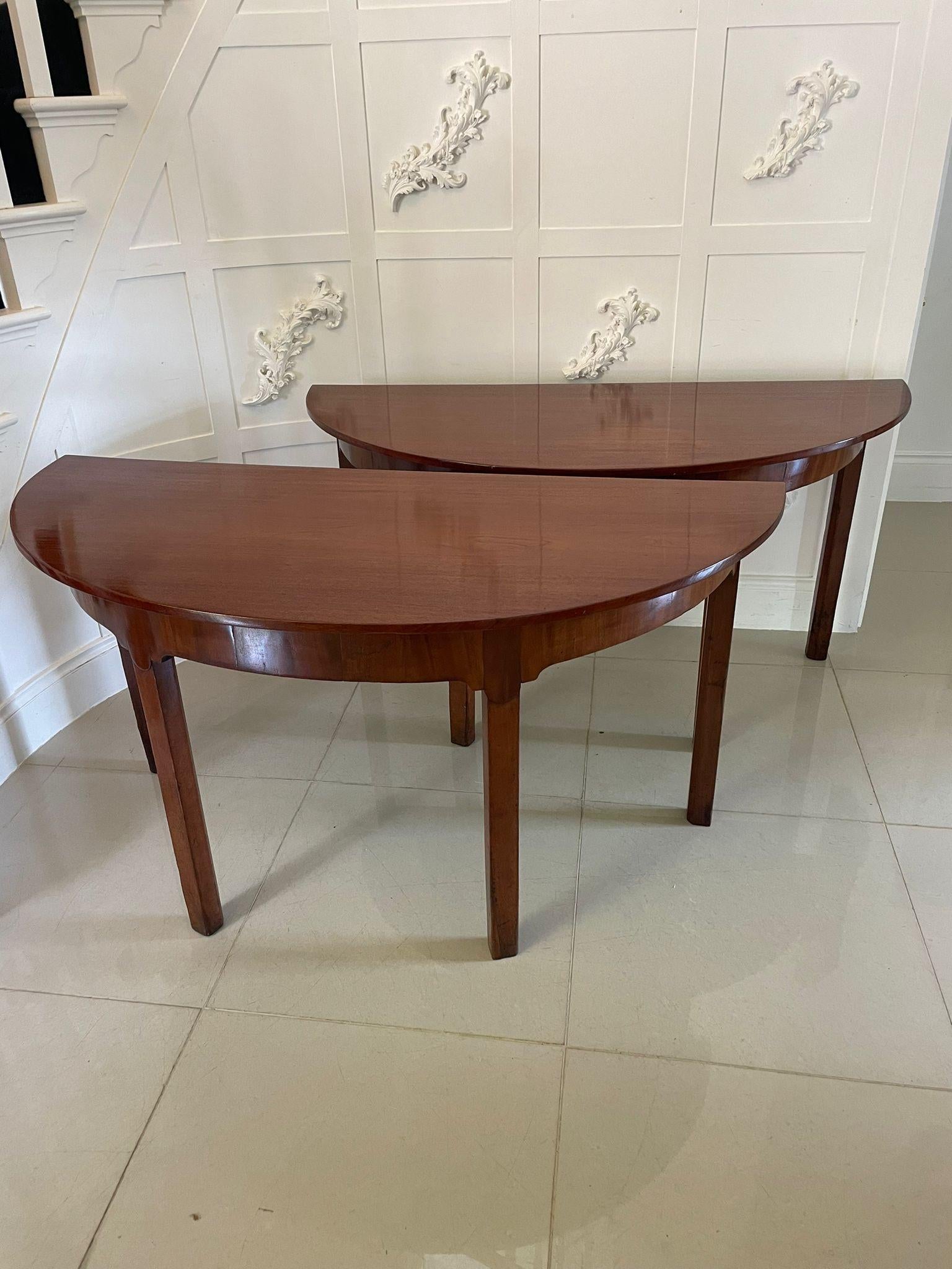 Pareja de consolas antiguas de caoba labrada de calidad Jorge III en forma de demi lune con tablero de caoba labrada de calidad en forma de demi lune sobre un friso de caoba labrada sobre cuatro patas cuadradas achaflanadas con una inusual y
