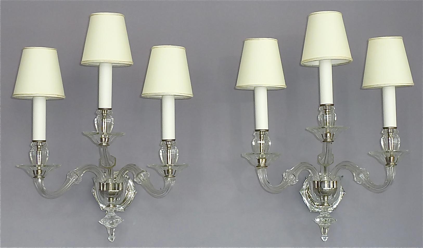 Large precious pair of classical Art Deco scrolled 3-arm hand-cut faceted crystal glass sconces or wall lamps with off white lampshades in the style of Baccarat, France or Germany, circa 1920-1930. The beautiful handcrafted crystal glass wall lights