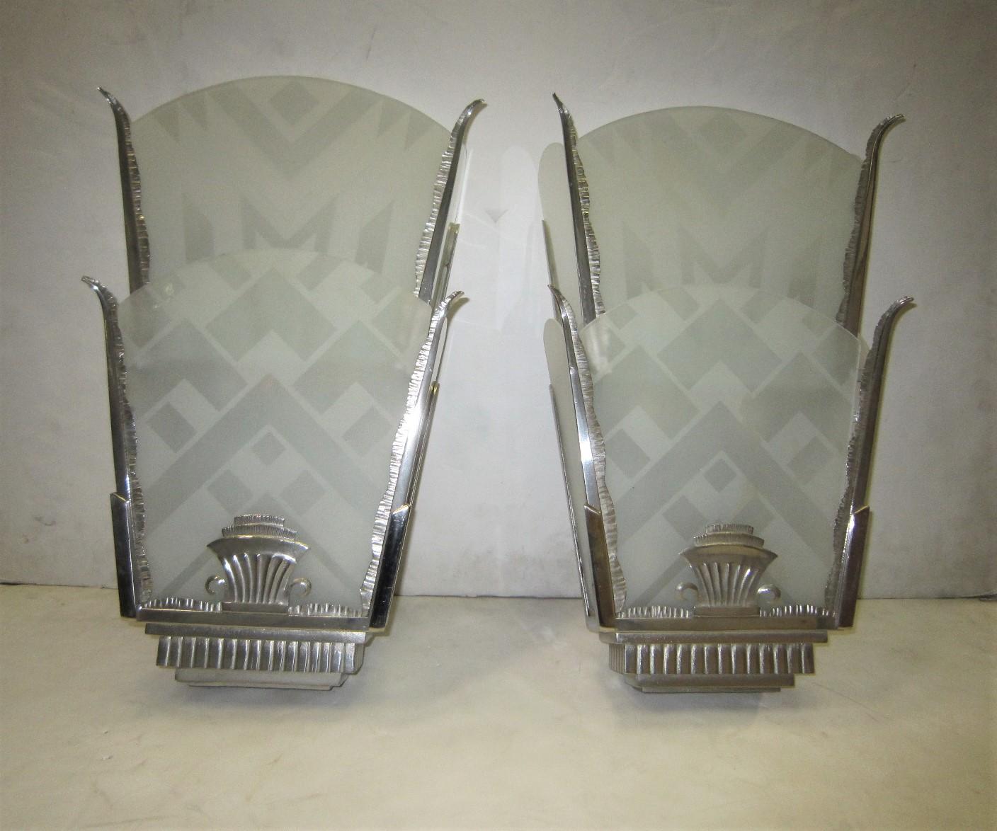 A pair of very large and spectacular Art Deco etched glass and nickeled iron wall lights.
Graceful leaf-like hand-hammered iron arms hold bi-level geometric motif etched glass panels.
The front etched panels with 