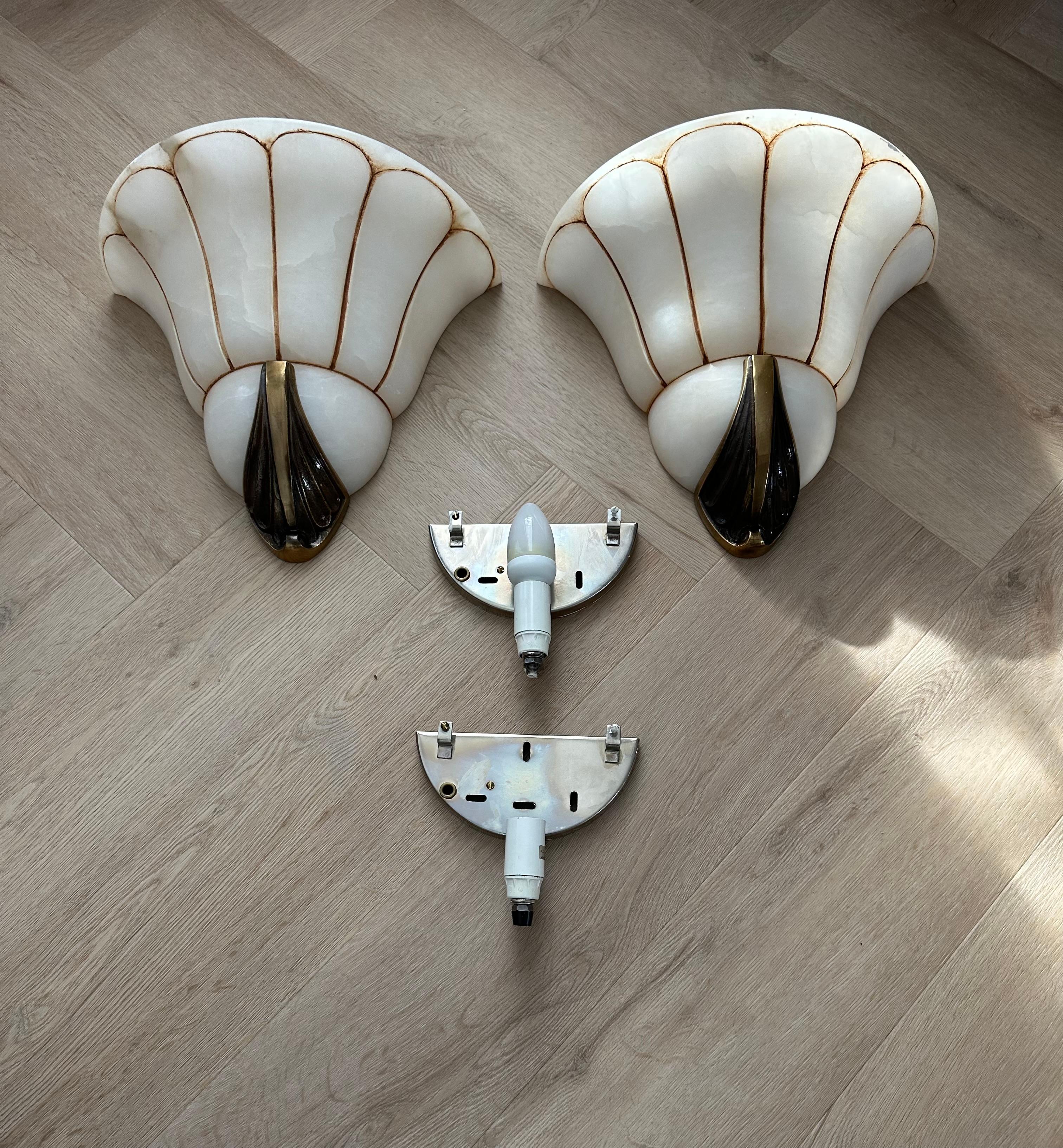 Excellent condition sconces with a marvellous carved pattern and hand painted lining in the stunning alabaster shades.

This unique pair of alabaster sconces is beautiful in shape and large in size. Hand-crafted with a bronze bracket decoration at