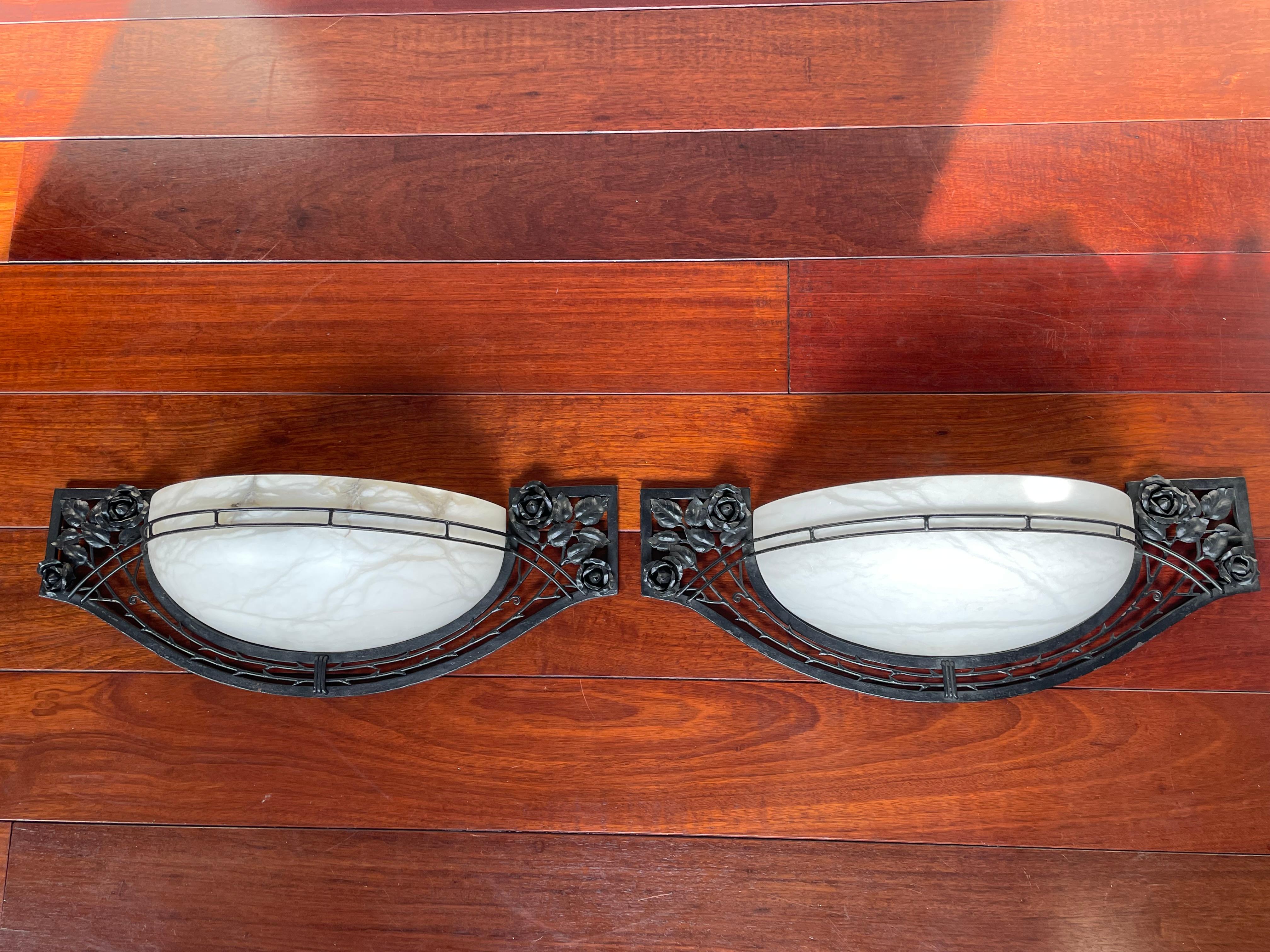 Impressive pair of sizable wall sconces with stunning alabaster shades.

This rare pair of Art Deco style sconces is beautiful both in design and execution. The combination of the blackened wrought iron with the hand-crafted rose motifs and the