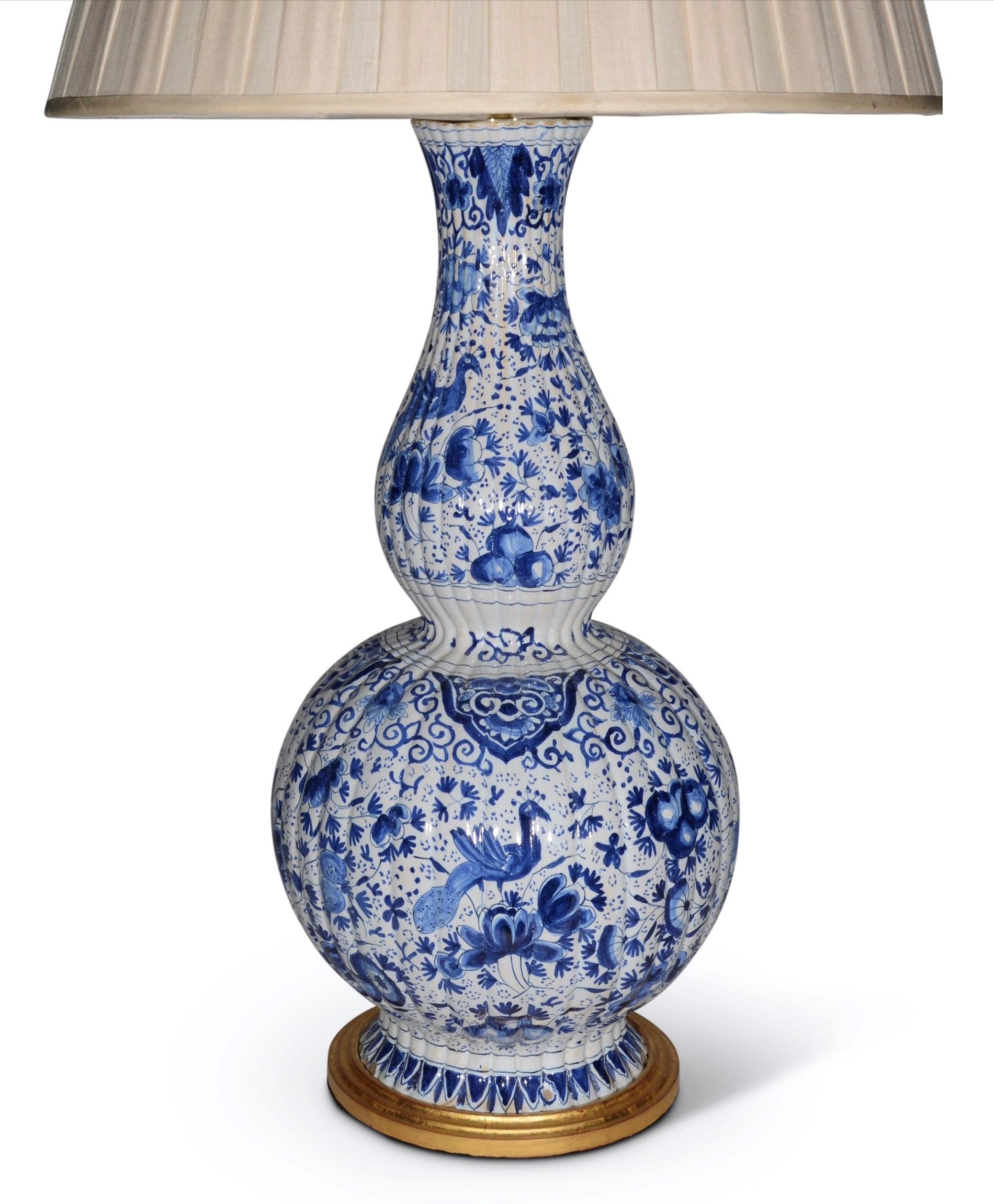 A magnificent pair of  large Dutch Delft vases. Of double gourd form, and decorated throughout with exotic birds amongst stylised floral and foliate decoration in tones of blues on a white background. Now mounted as lamps wit hand-gilded turned