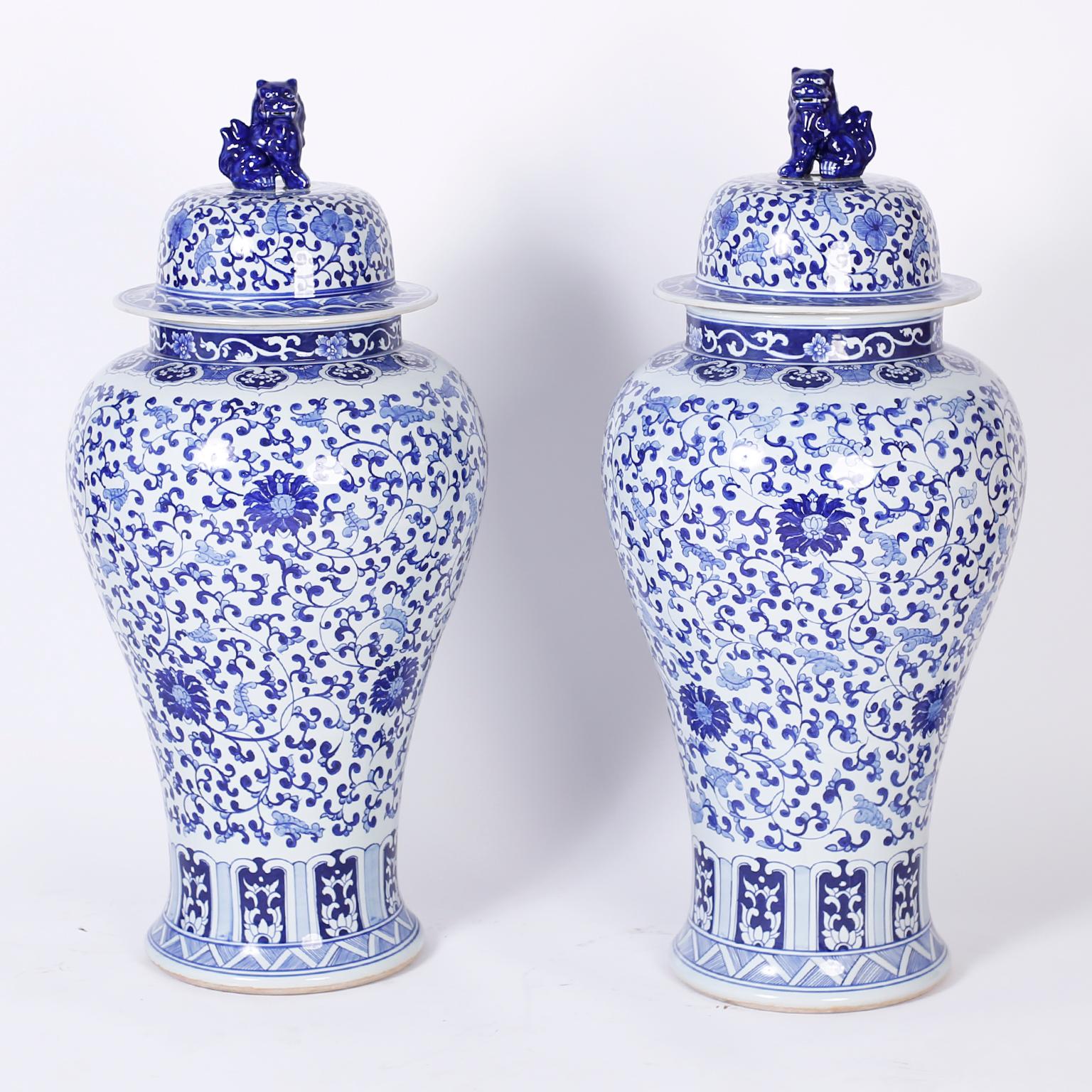 Impressive pair of Chinese blue and white urns hand decorated in delicate floral vine and leaf designs punctuated by flowers and featuring cobalt blue foo dog lid handles.