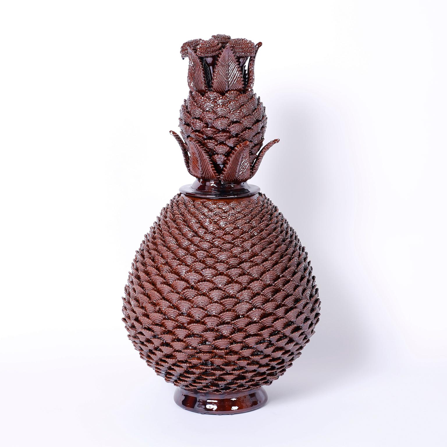 With a striking display of pottery brilliance, this pair of glazed terra cotta stylized pineapple jars feature slightly different floral clusters on the lids and repeating husks or shells wrapped around the entire body. 

Height varies by 1