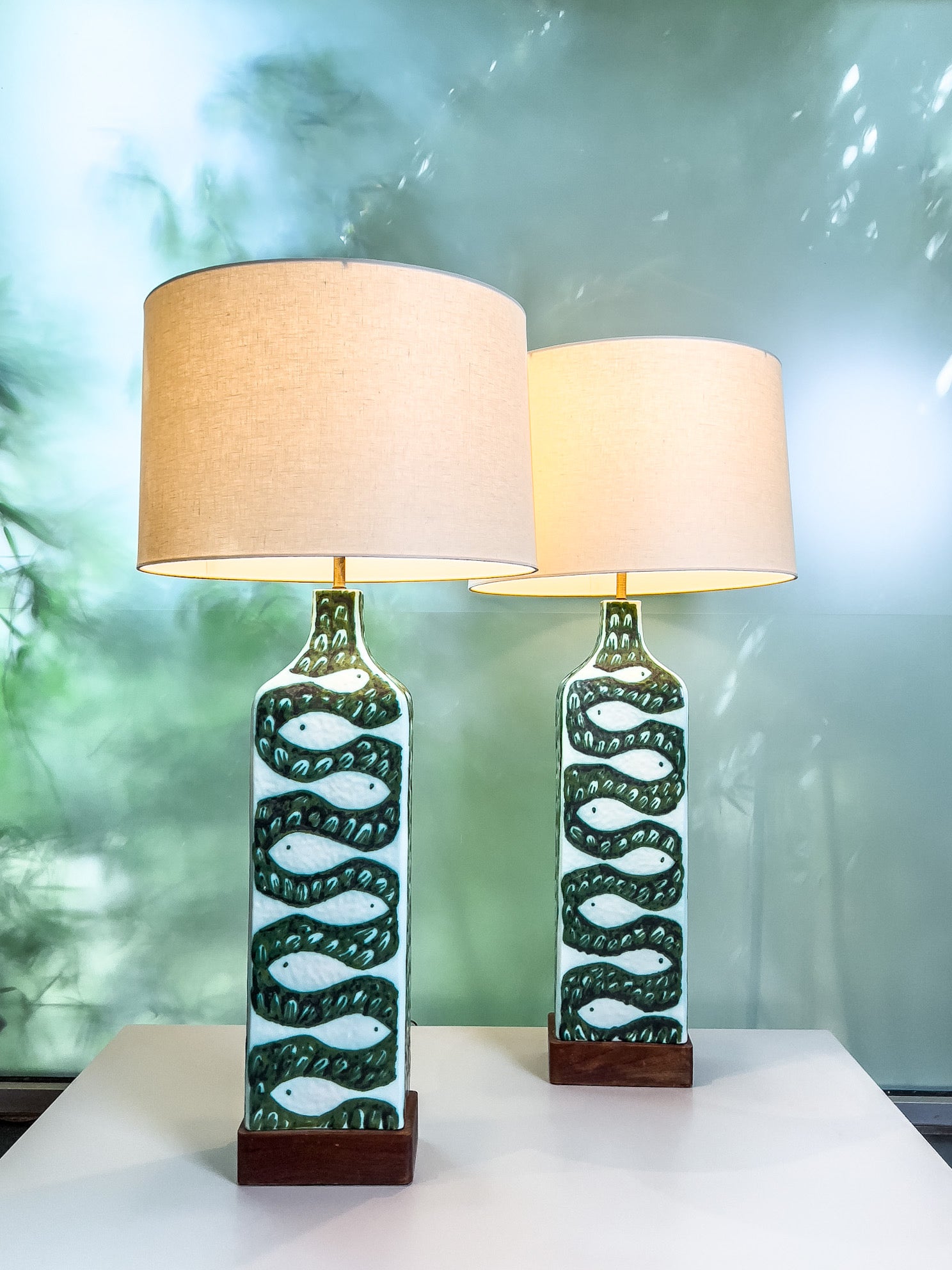 A large pair of ceramic lamps with birds on one side and fish on the other sitting on a walnut base. Designed by Alessio Tasca for Raymor. Rewired.
