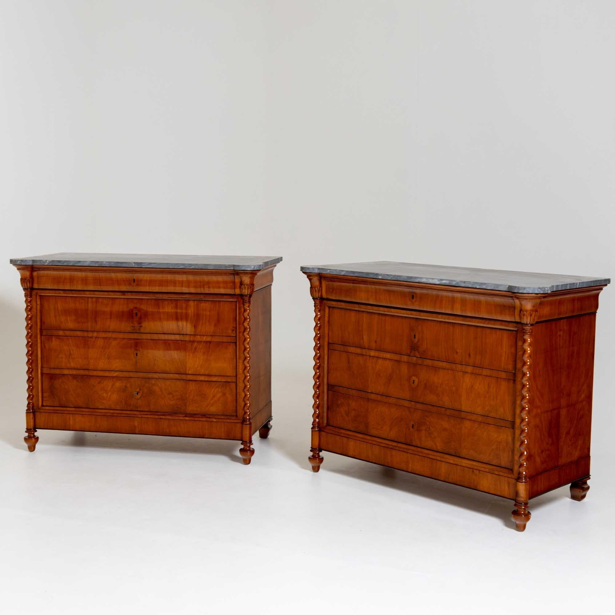 Pair of large chests of drawers in solid and veneered cherry wood with grey stone tops. The chests stand on baluster feet that develop into turned columns with leaf capitals, giving the chests a rounded corner solution. The three lower drawers with