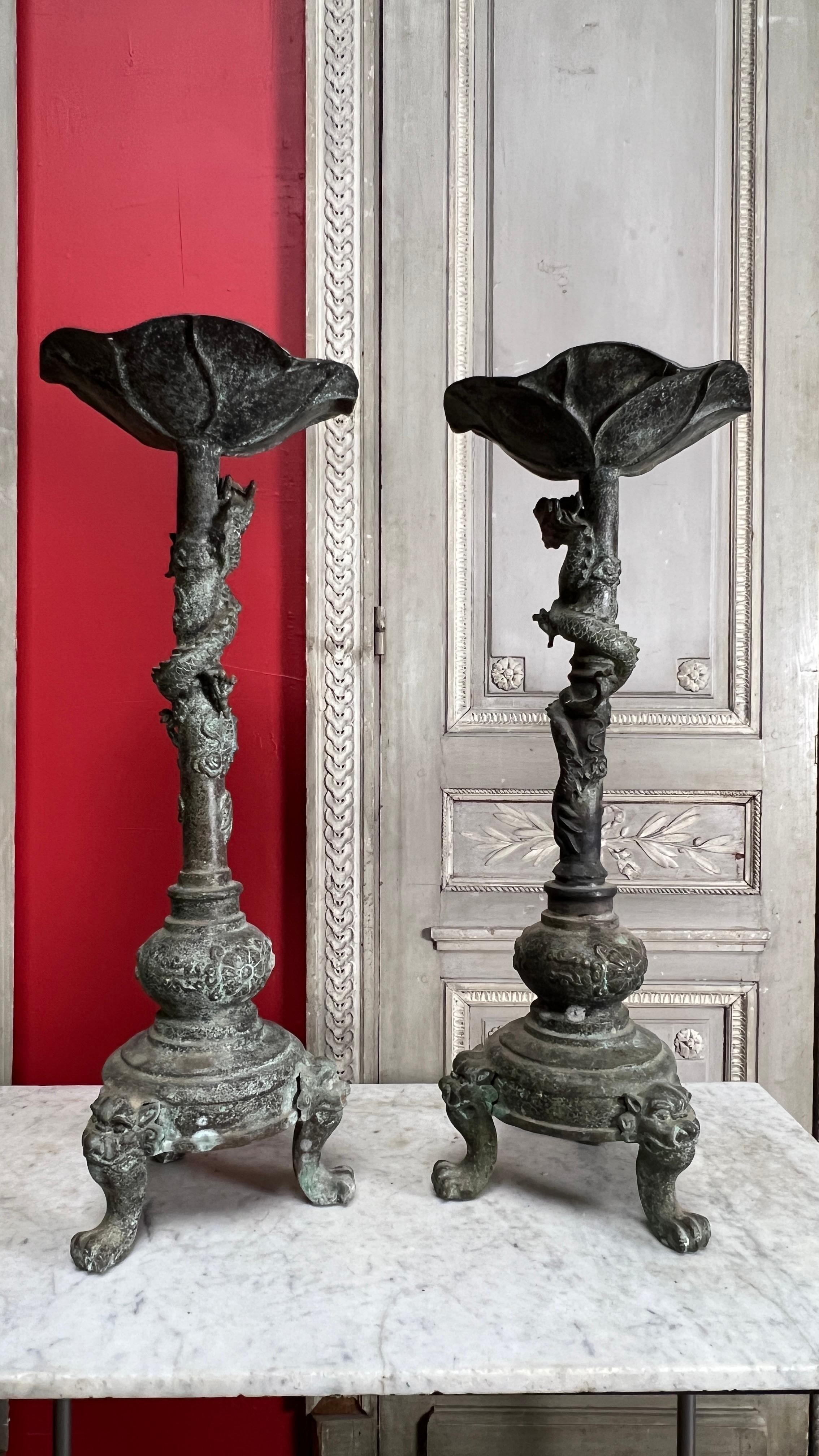 A large pair of Chinese bronze  candle stands candlesticks in a patinated and verdigris finish.  These large and impressive candle holders have three foo dog legs and a dragon wrapped around the column, topped with a lotus. 
They are highly