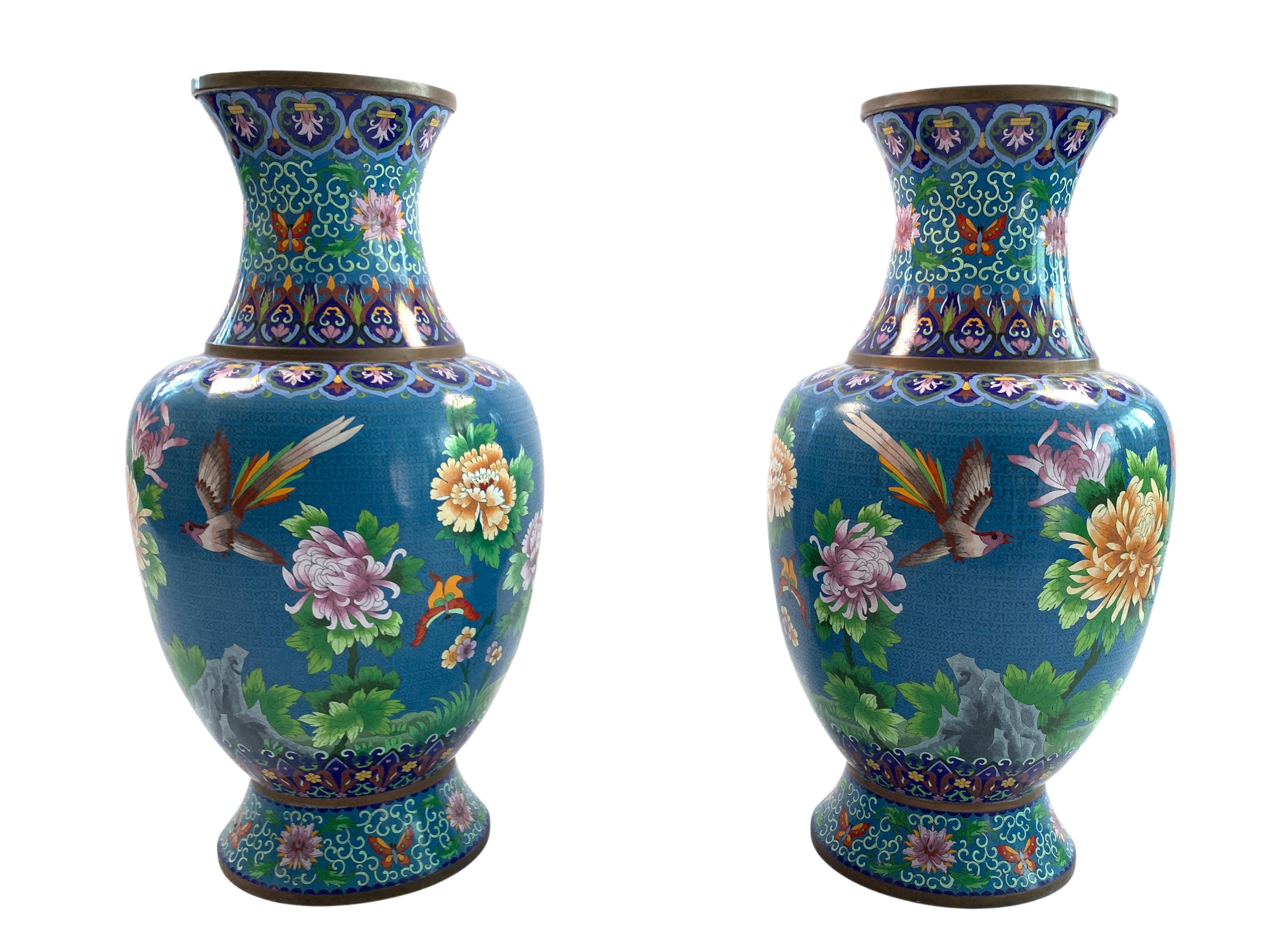 A lovely 20th century pair of brass Chinese Cloisonné vases sites on gilded wooden bases. Decorated with a striking blue enamel ground with red, yellow and pink chrysanthemum flowers and birds, collar and footed base are decorated with Cloisonné