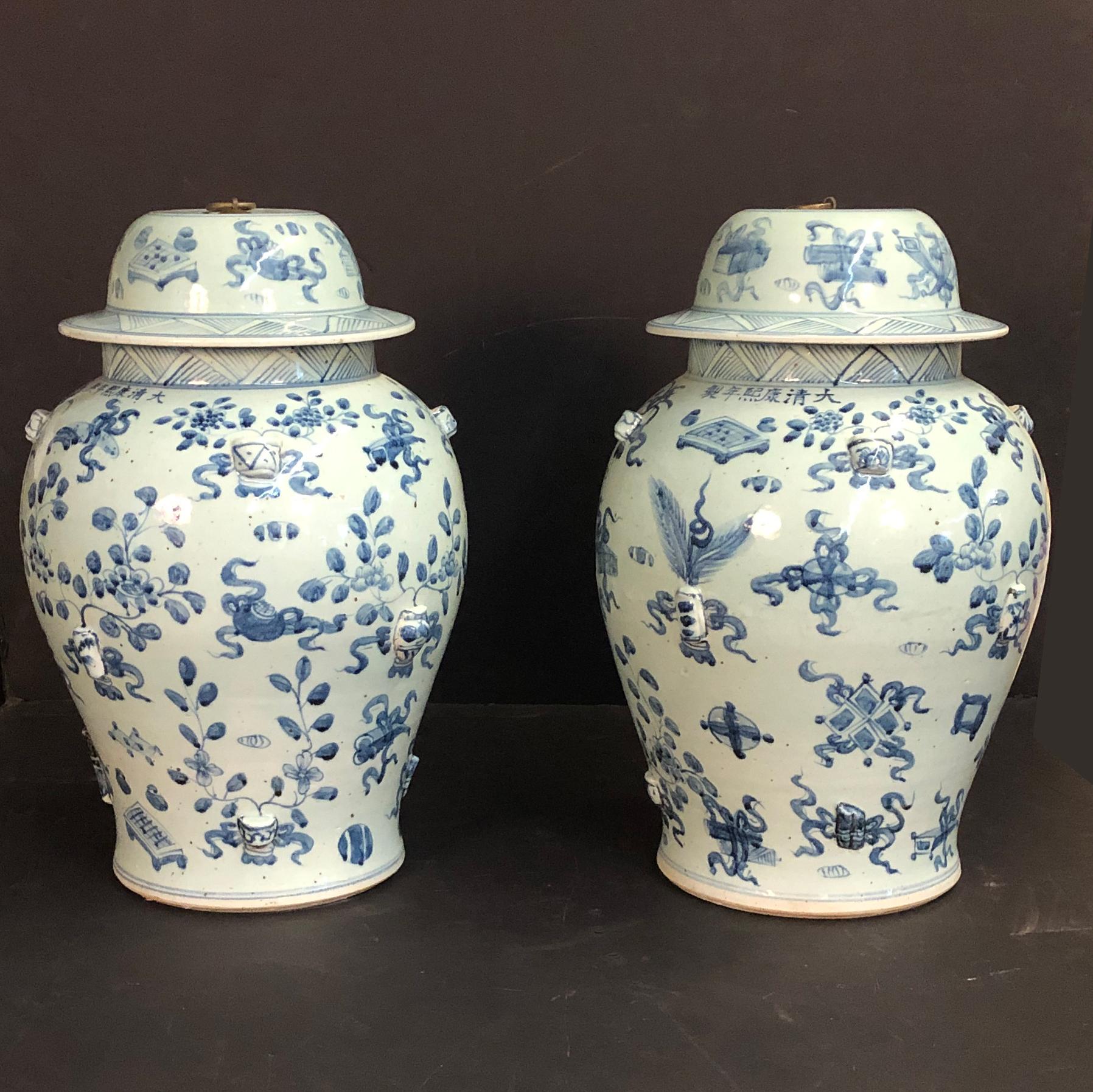 A large pair of blue and white hand painted ceramic lidded temple jars with metal ring turn handle and decorated with floral motifs and still life scenes.