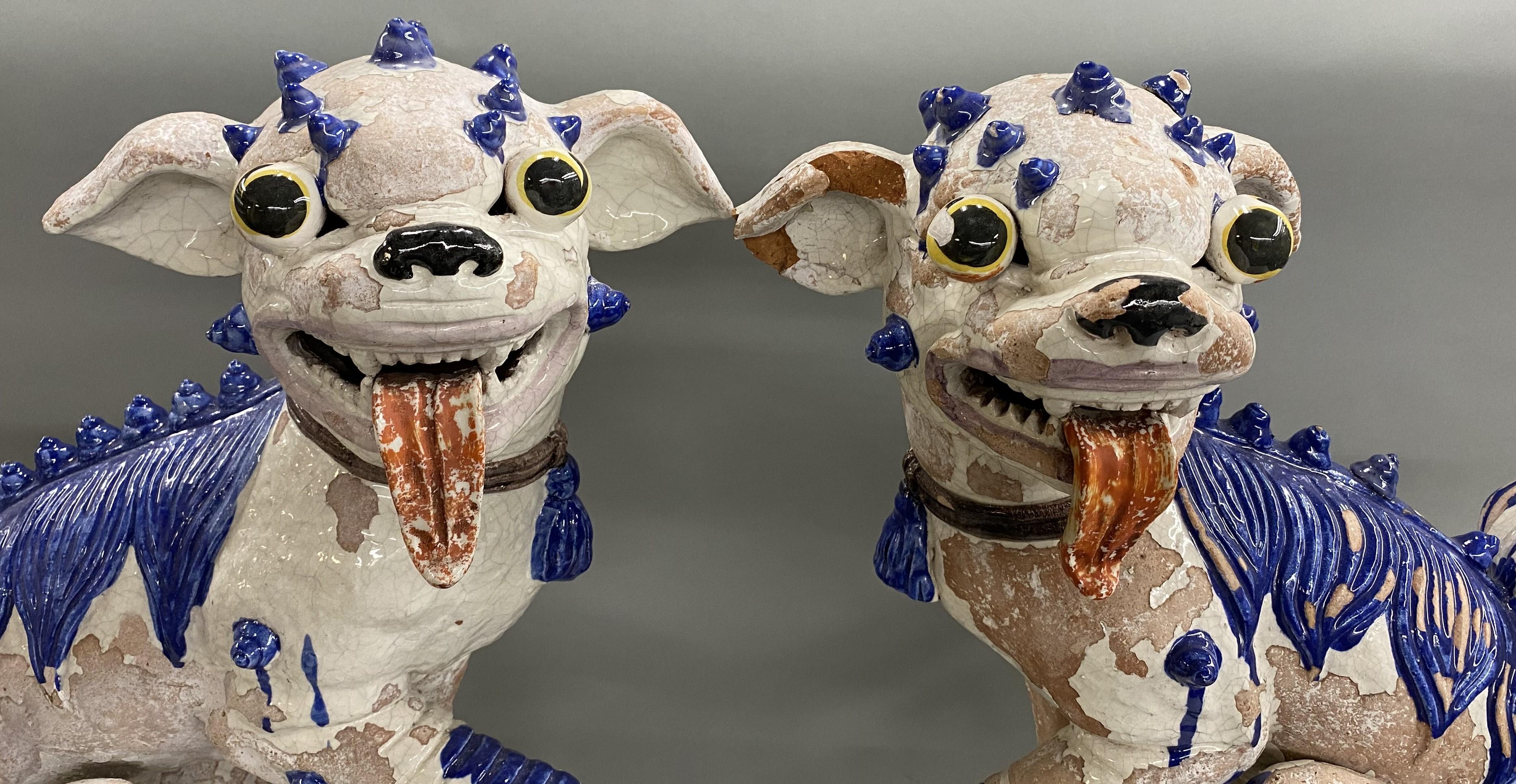 A large pair of Chinese tin glazed pottery or earthenware Foo Dogs, one with a ball under his paw and the other with a small pup. The pair date to the 20th century, with noticeable surface glaze losses, some corner losses, craquelure throughout, and