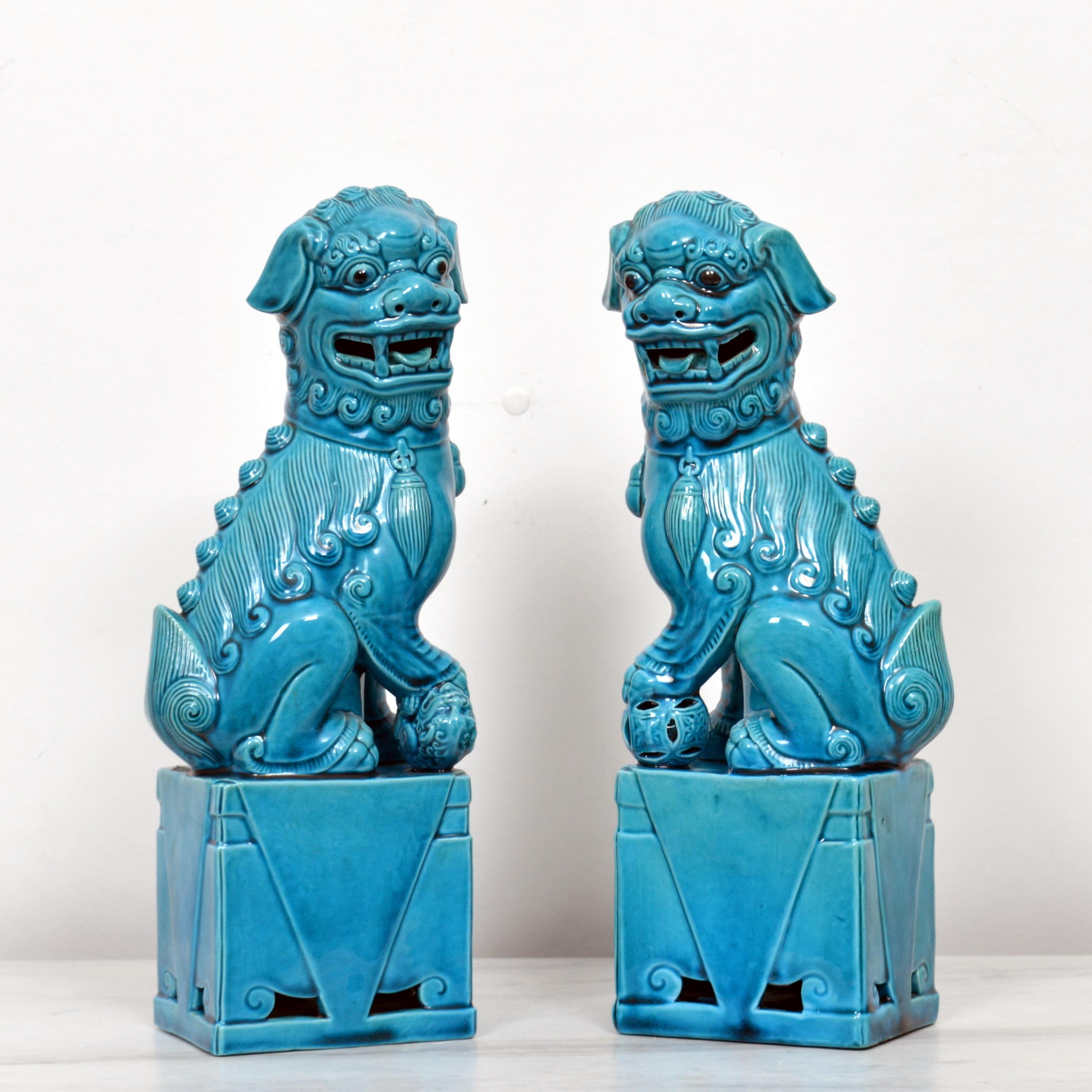 A very fine and detailed pair of Chinese turquoise glazed foo dogs. The hollow biscuit porcelain figures stand raised on a rectangular base and are looking sideways with open mouths and tongues showing teeth each with a raised front paw, one resting