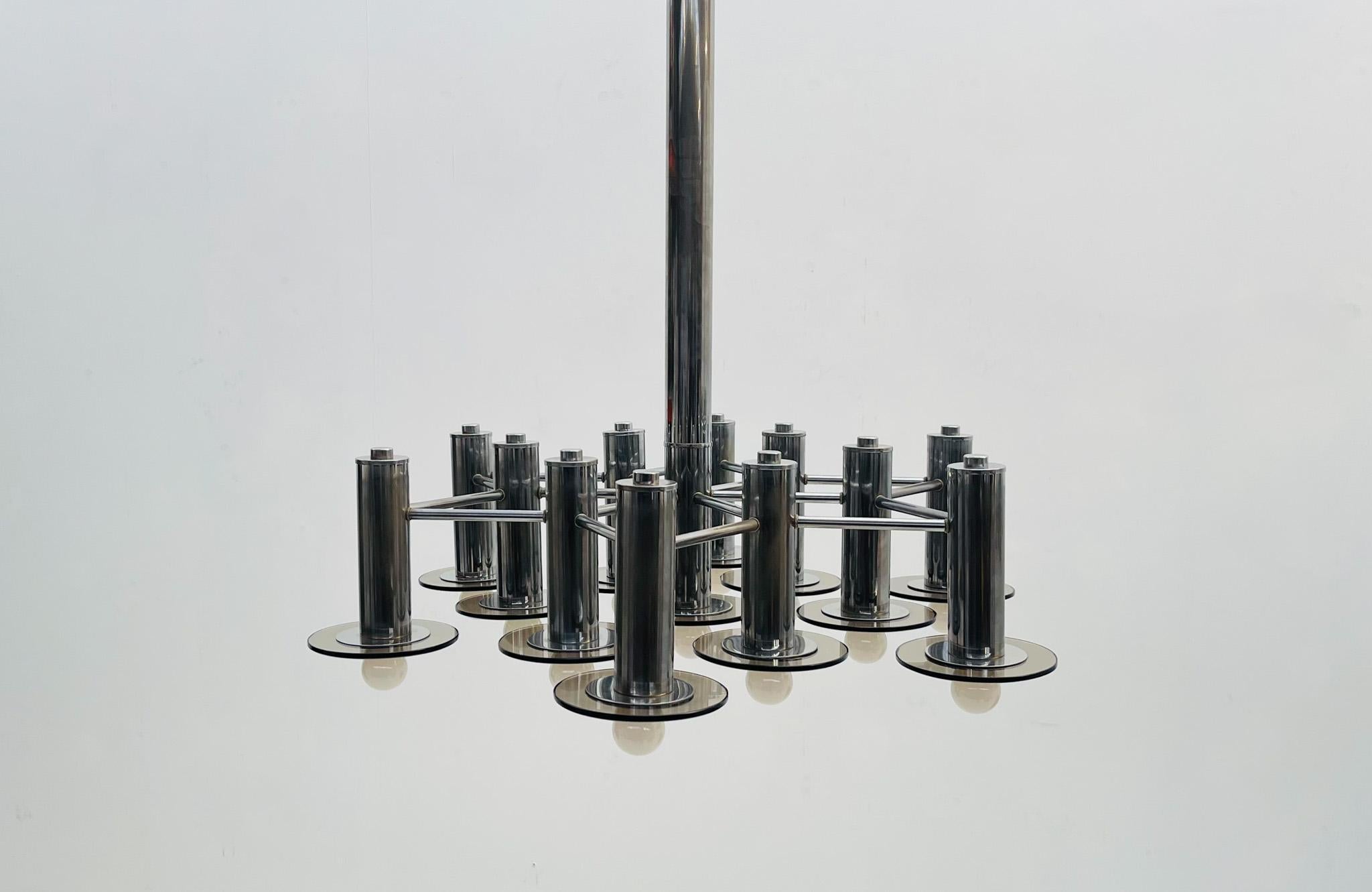 Questa sorprendente coppia di lampadari della metà del secolo scorso presenta un'elegante struttura cromata abbinata a elementi in vetro fumé, creando un'estetica audace e moderna. Ogni lampadario è composto da una disposizione simmetrica di bracci