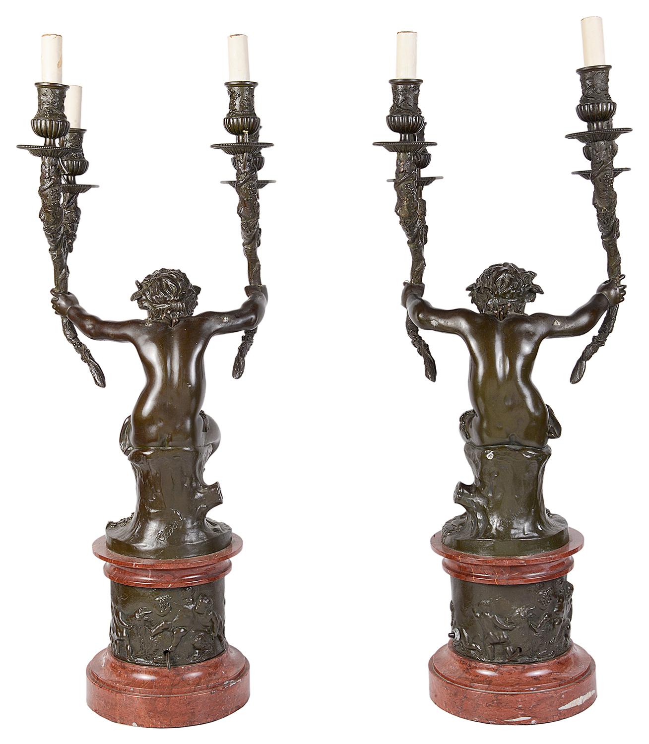 A good quality pair of 19th century bronze two branch candelabra, each with a smiling Putti with leaves and grape head bands, out stretched arms holding four branch like candle sconces, mounted on Rouge marble plinths and a bronze relief band round