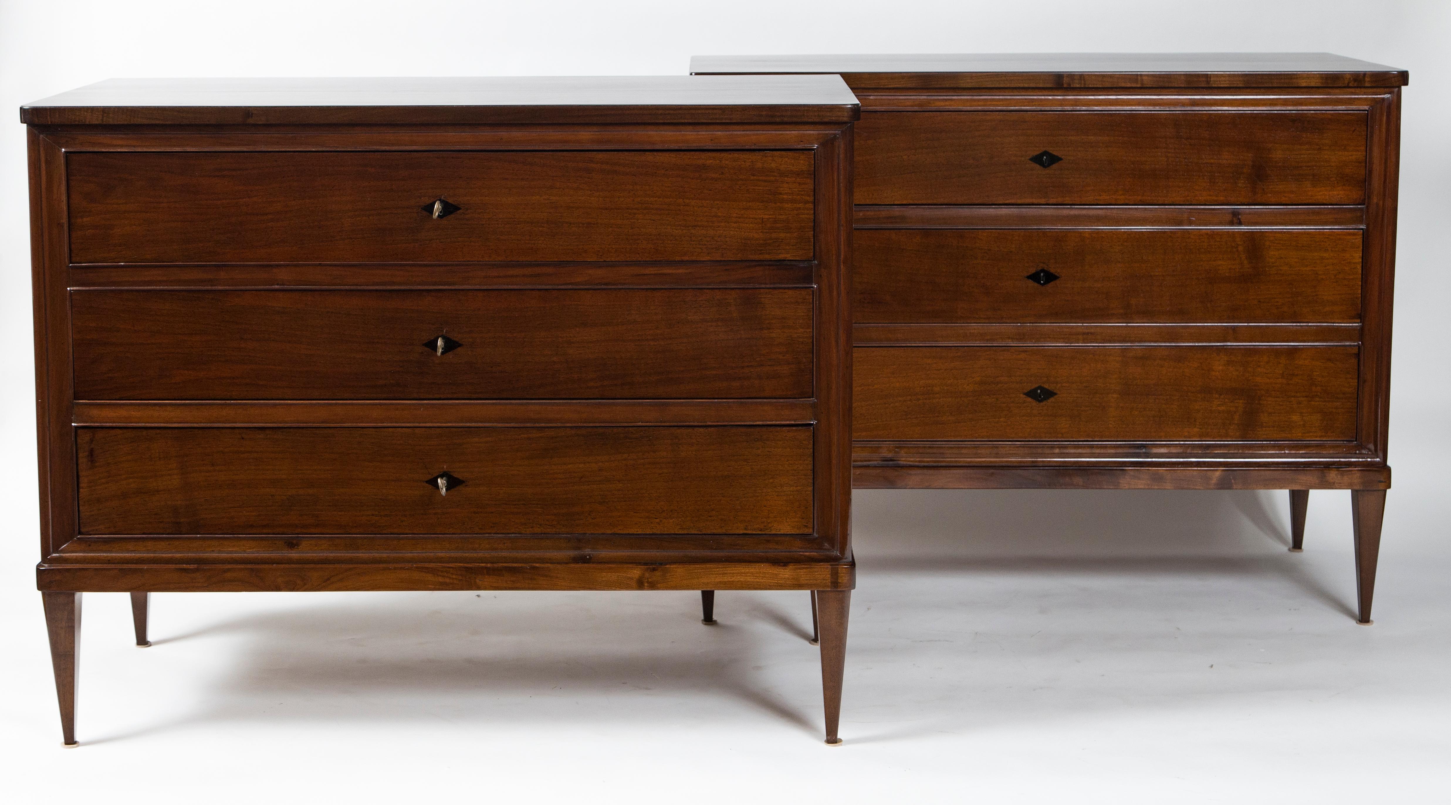 Pair of sleek Italian chests comprised of three drawers finishing on straight and tapered legs in a dark stained solid walnut wood, adorned with darker stained inlaid diamond-shaped escutcheons, a working key for each drawer is provided
Origin: