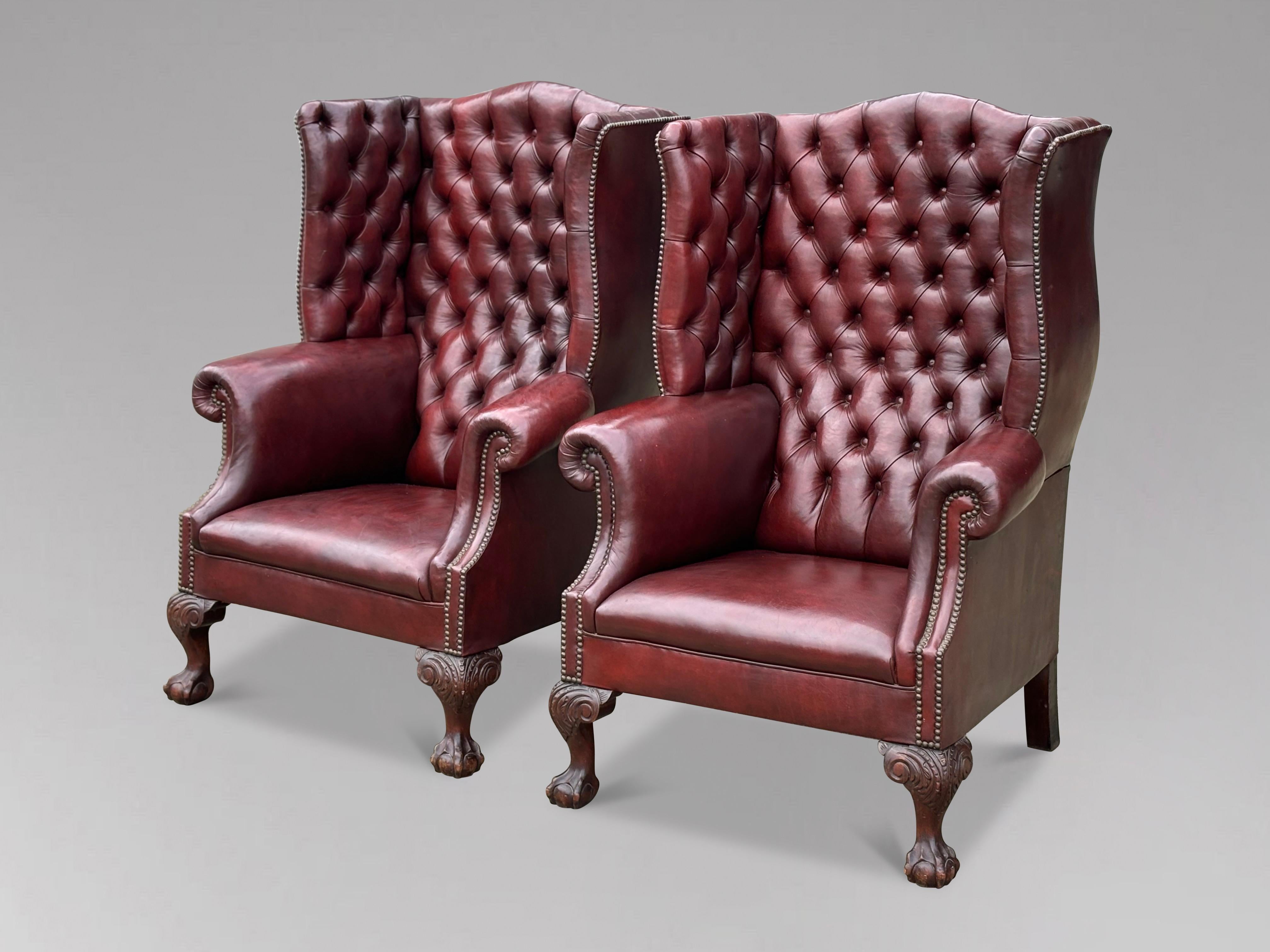 Un par de excepcionales sillones de orejas de cuero color sangre de principios del siglo XX, de estilo Jorge III, que conservan su elegancia original e intacta. Los armazones, sustanciosos y bien proporcionados, presentan una tapicería de botones