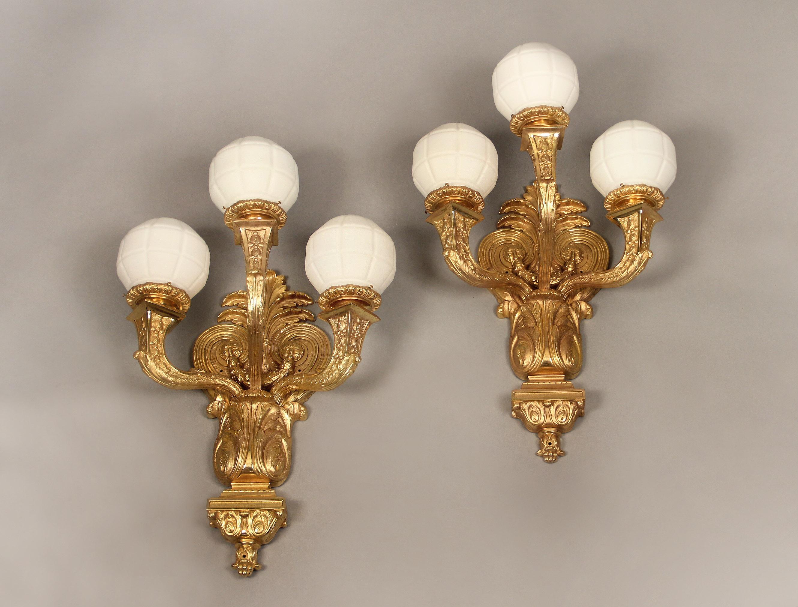 A large pair of early 20th century gilt bronze three-light sconces

A heavily chiseled foliate back plate and three strong arms with white glass globes.