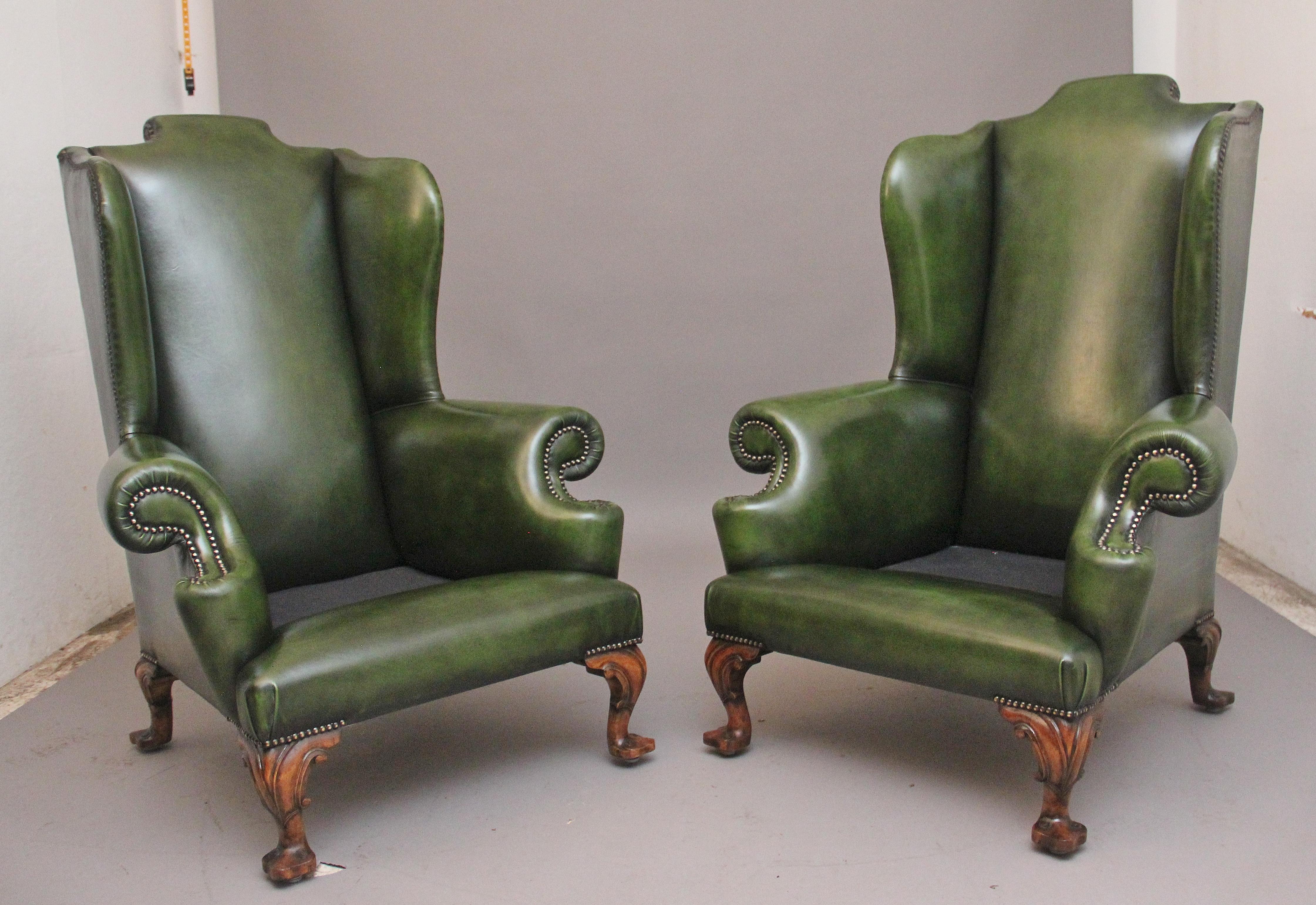 A fabulous pair of large early 19th Century walnut wingback armchairs in the Georgian style, just been reupholstered in a green leather with brass stud decoration, having a shaped high back with winged sides coming down to the curved arm supports,