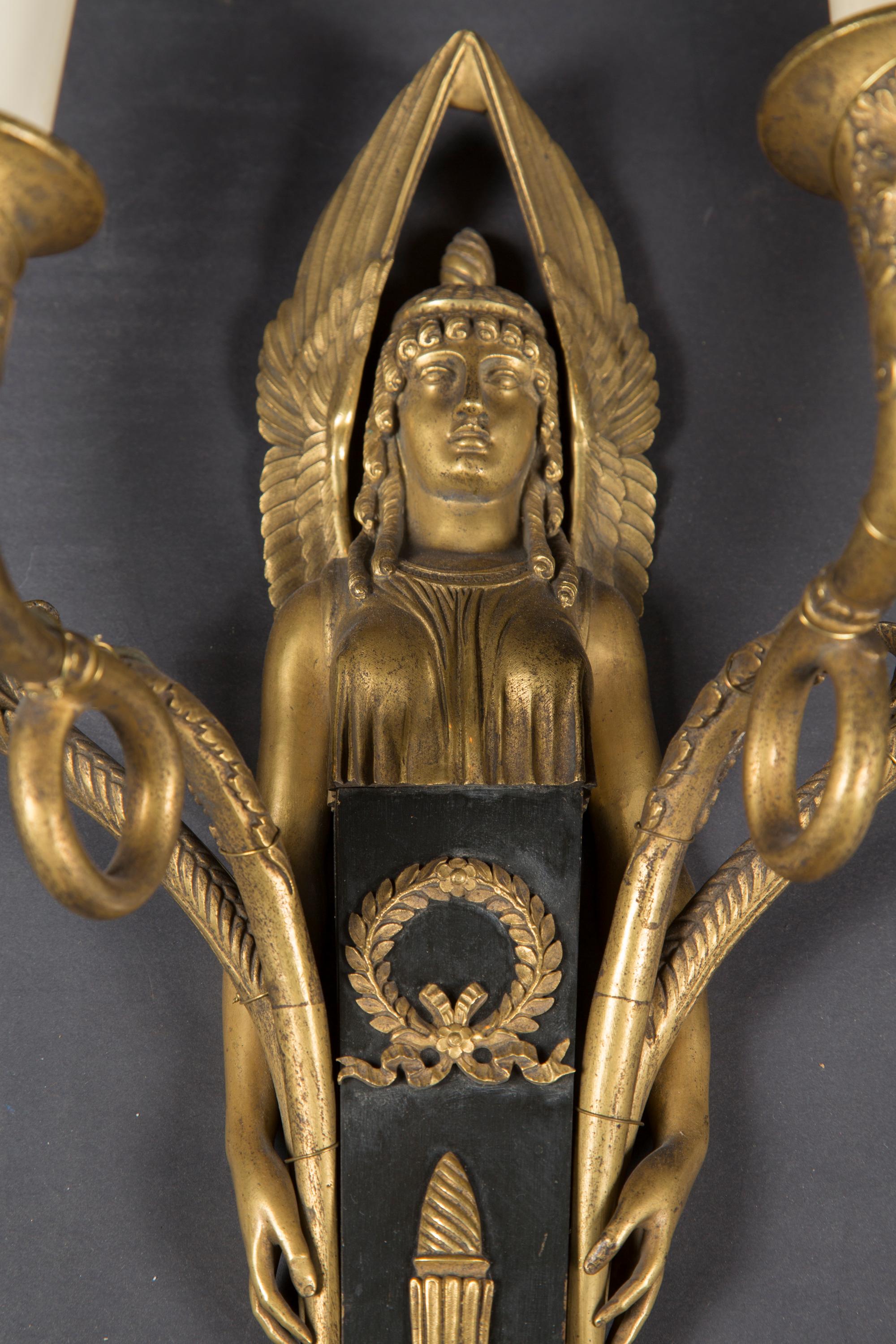 This gorgeous pair of 19th century Empire sconces are made of bronze and tole, and feature fantastically stylized Egyptian figures on each back plate. Note the details in the wings, the fabric and hands with fingers resting on the arms. The canter