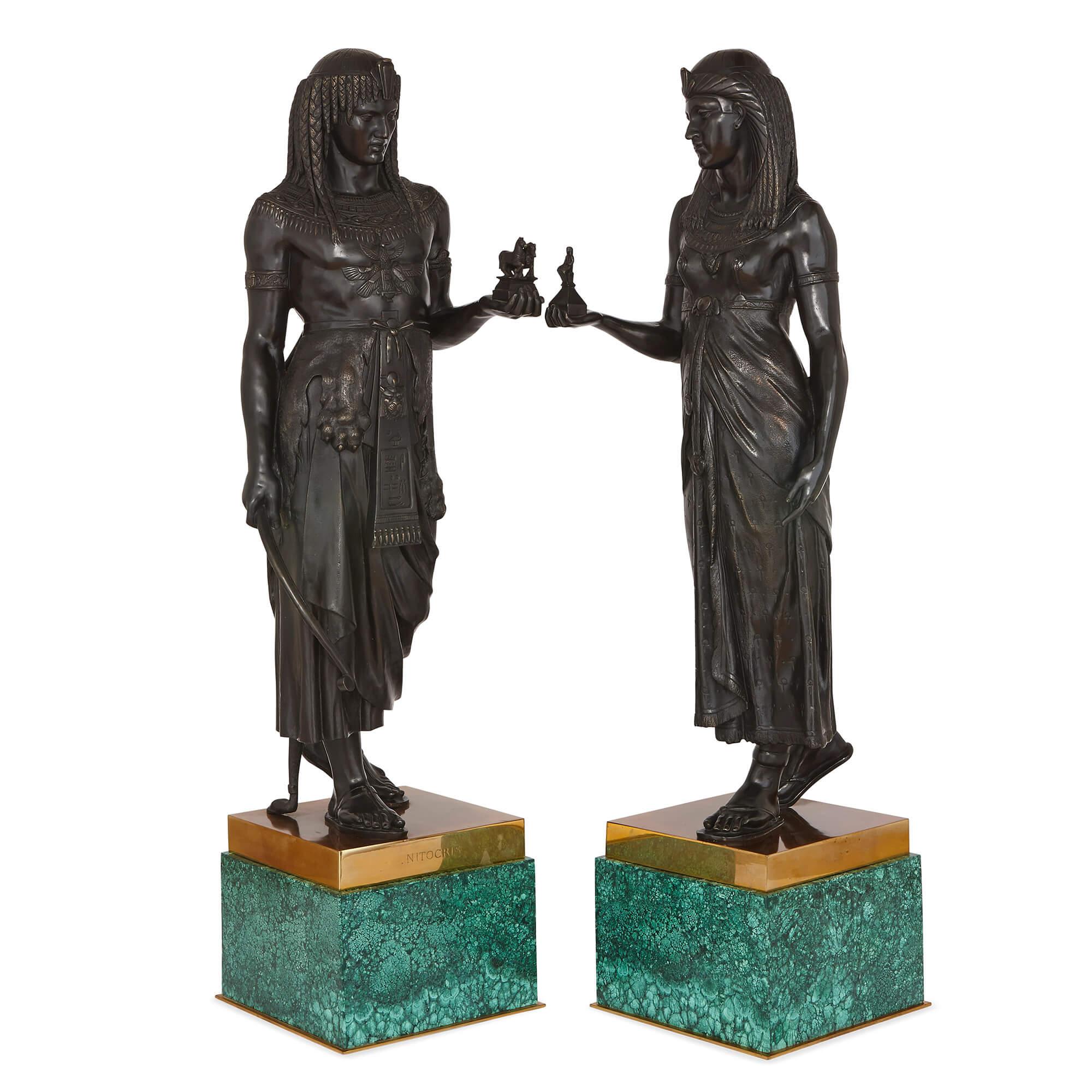 The pair of figures, one male and one female, are cast in patinated bronze, and are styled as Egyptian figures in the Empire style of Napoleon I. The sculptures are set upon square-form gilt bronze plinths, themselves mounted onto striking green