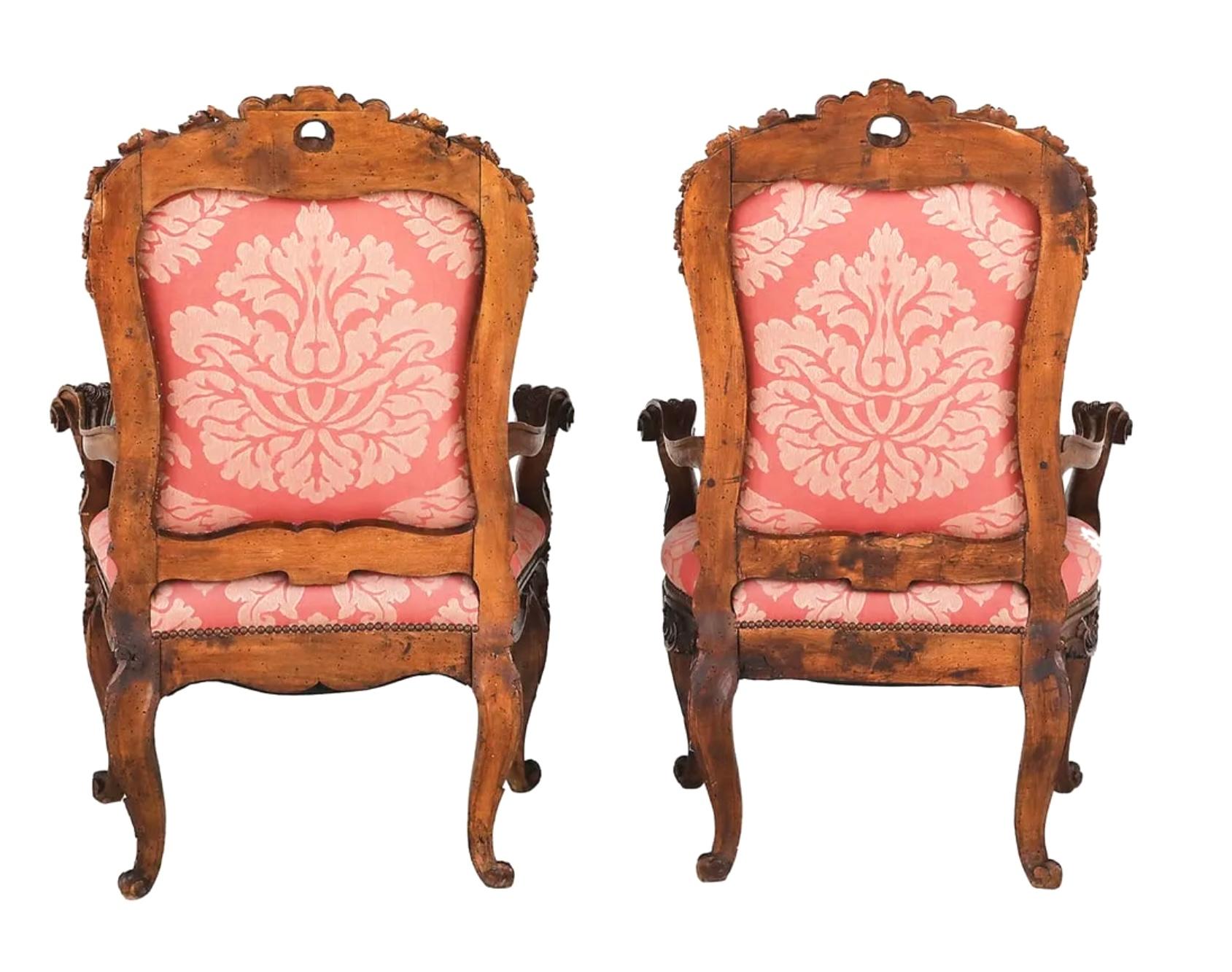Late 19th century large pair of Italian Armchairs.  Each exuberantly carved example with a padded back surmounted by a pierced foliate and floral crest, joined by scrolling arms to the like seat, raised on cabriole legs ending in scrolled toes. They