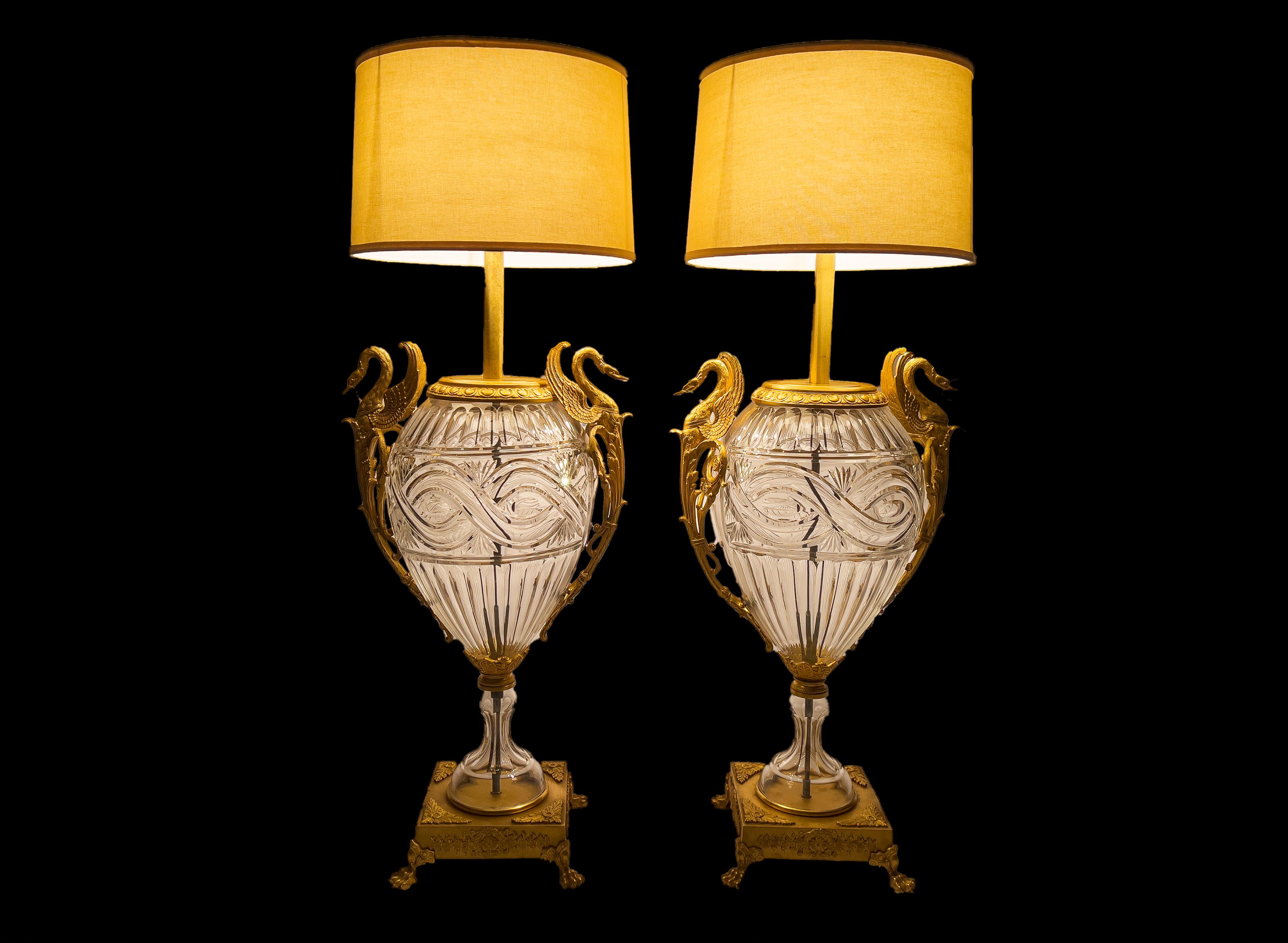 A fine large pair of cut glass vases fitted as lamps, Each with ovoid cut glass body flanked by winged swan handles, raised on square ormolu base with four paw feet.
     