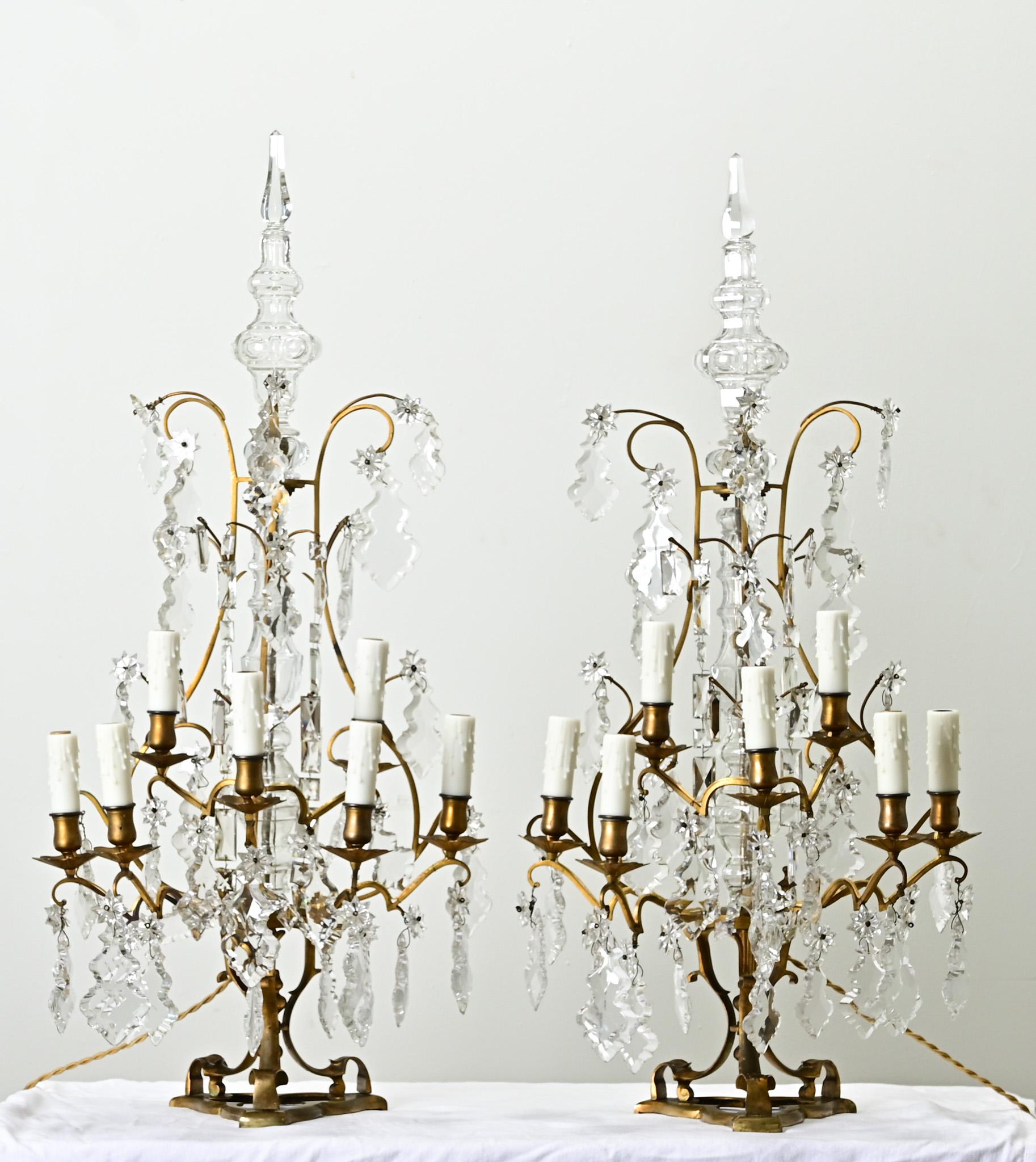 A massive pair of French 19th century brass and crystal girandoles also known as table chandeliers. This fine pair of glistening light fixtures have brass solid frames with seven scrolling candelabra arms and faux wax candle covers. Cut crystals
